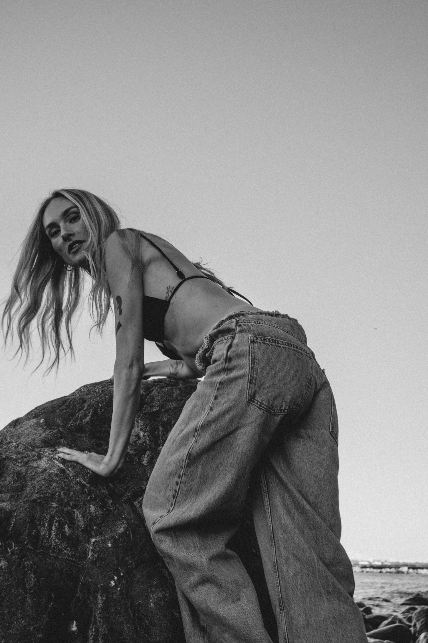Fashion model in denim poses artistically against rocks in black and white.