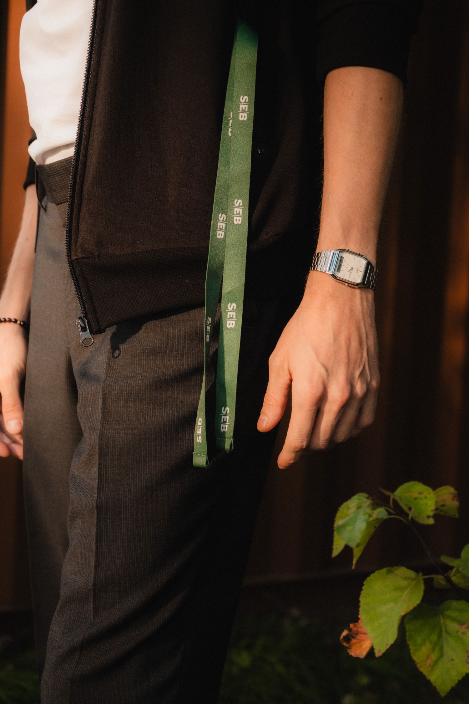 Close-up view of hands wearing a green wristband against a dark background with plant leaves visible.