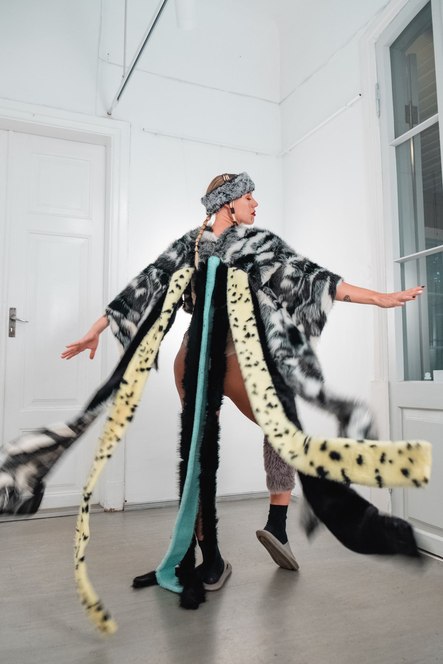 Dynamic fashion pose in flowing animal print coat and headwrap against white interior.