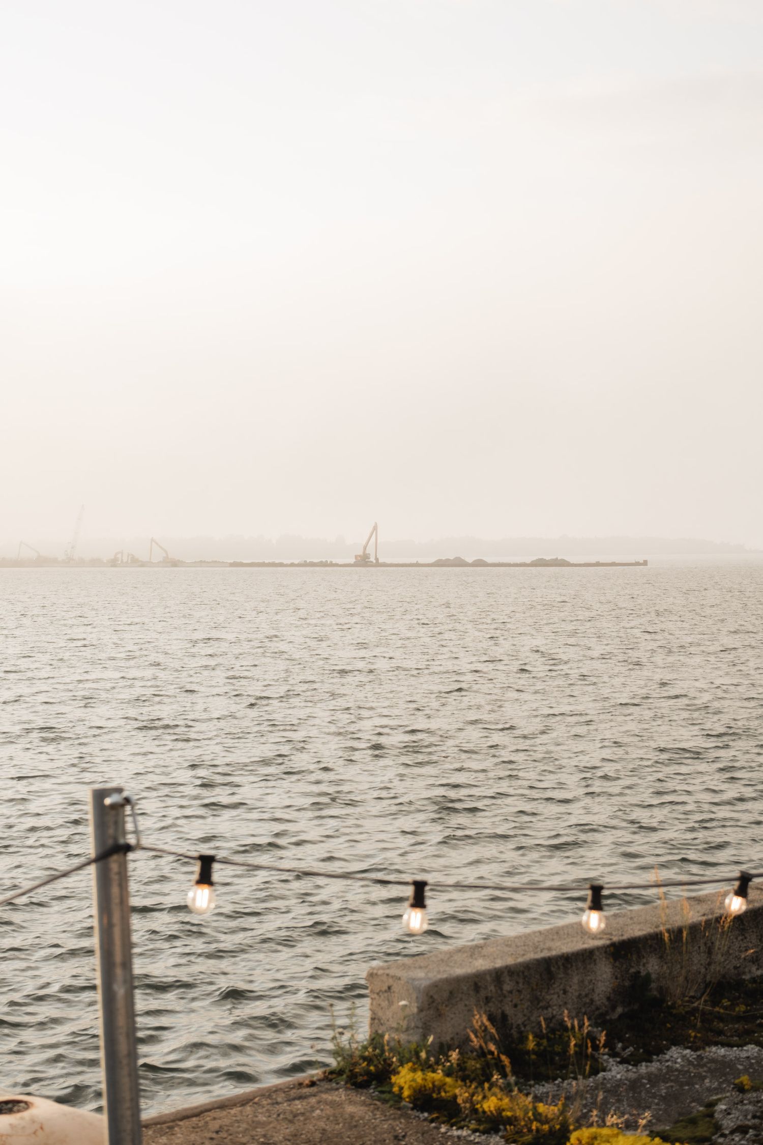 A misty seascape with string lights and a distant sailboat on the horizon.