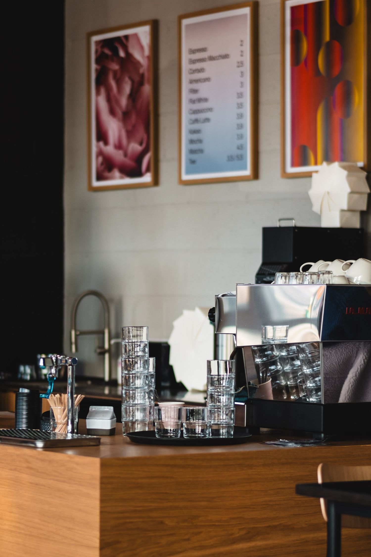 Modern coffee bar setup with framed artwork and professional equipment on wooden counter.