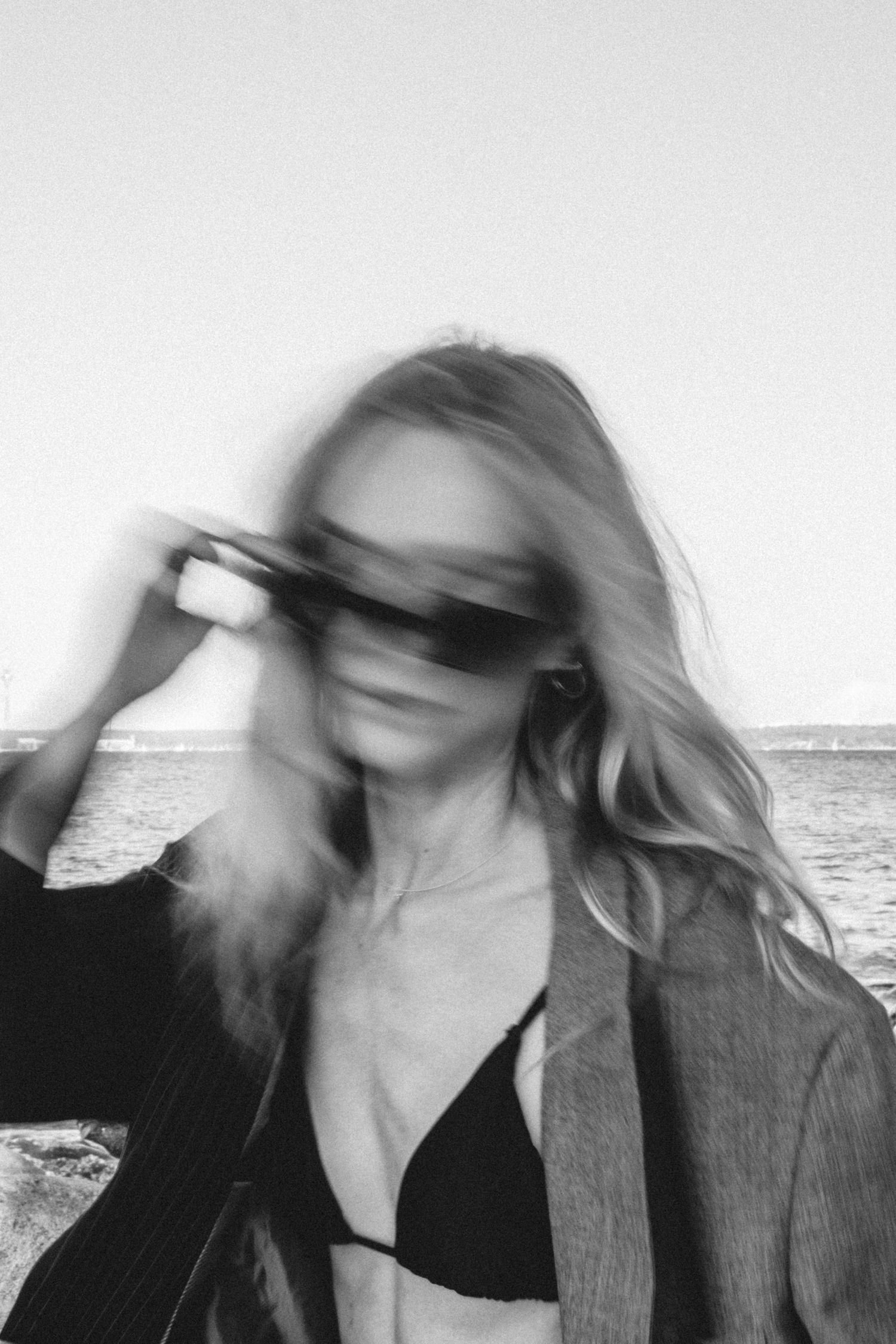 Artistic blurred motion portrait in black and white against seaside background.