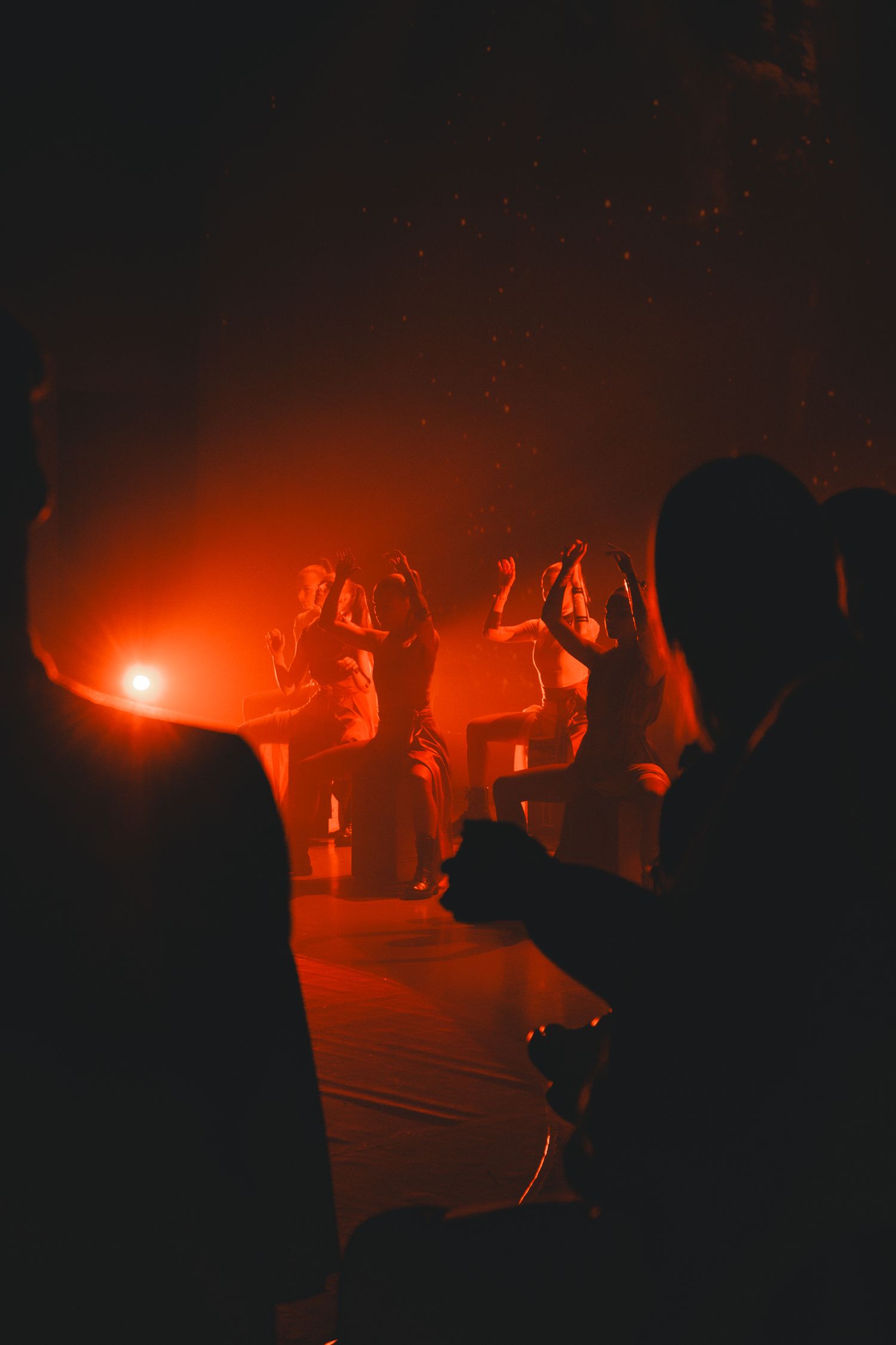 Silhouettes of performers illuminated by dramatic red lighting during a theatrical performance.