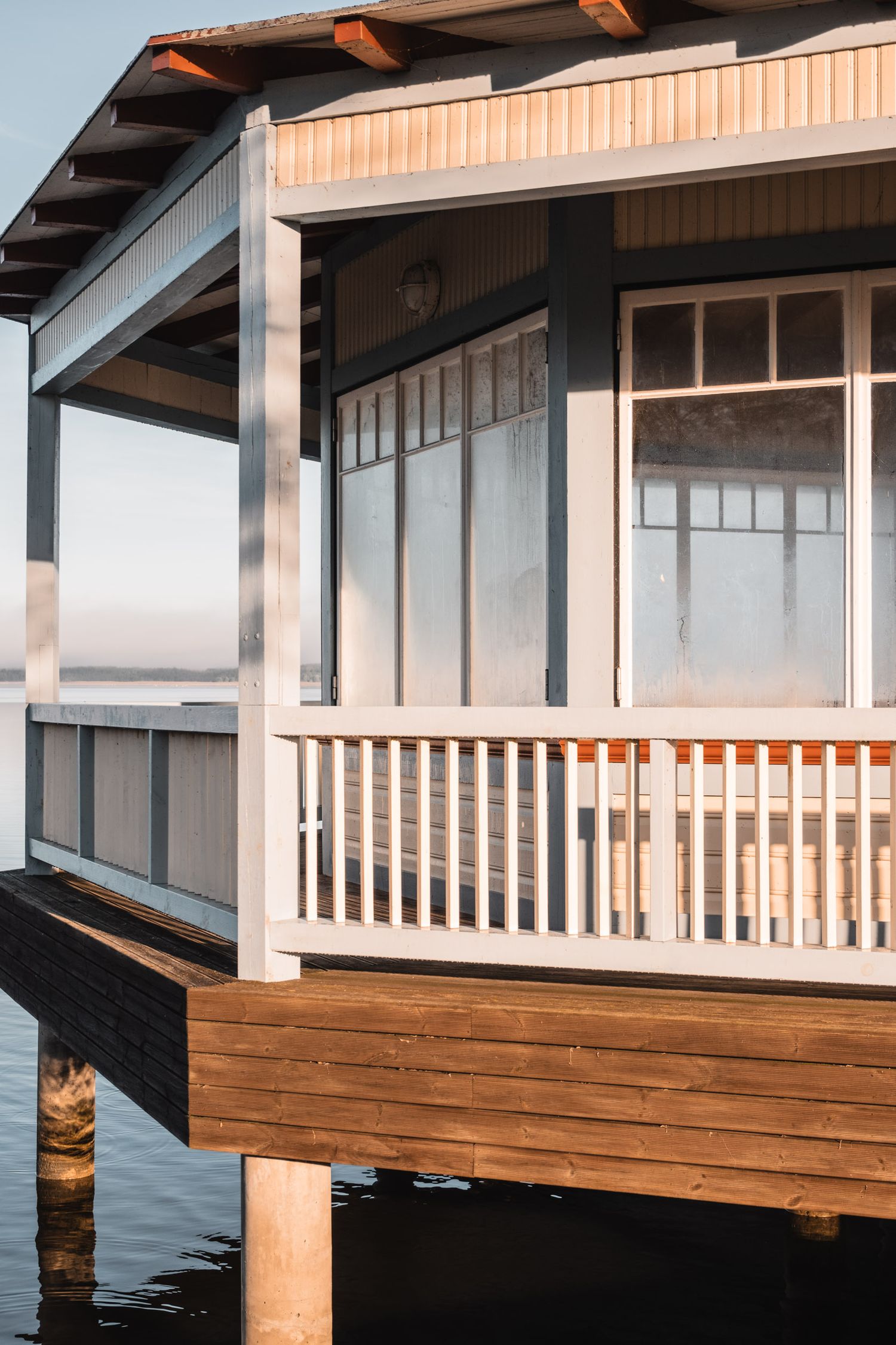 Modern waterfront house with white railings and large windows overlooking calm waters.