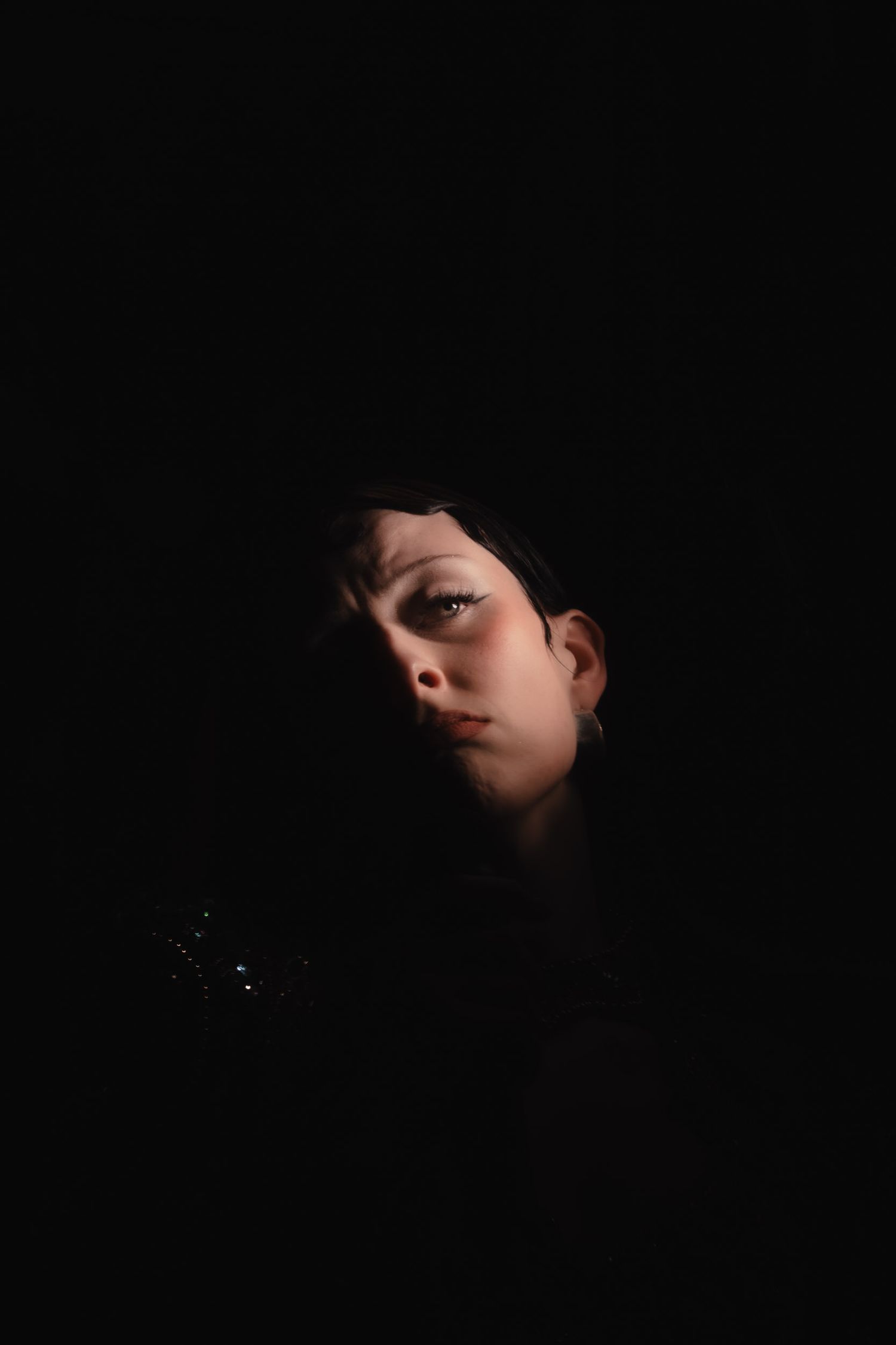 Dramatic low-key portrait emerging from darkness with strong shadow play.