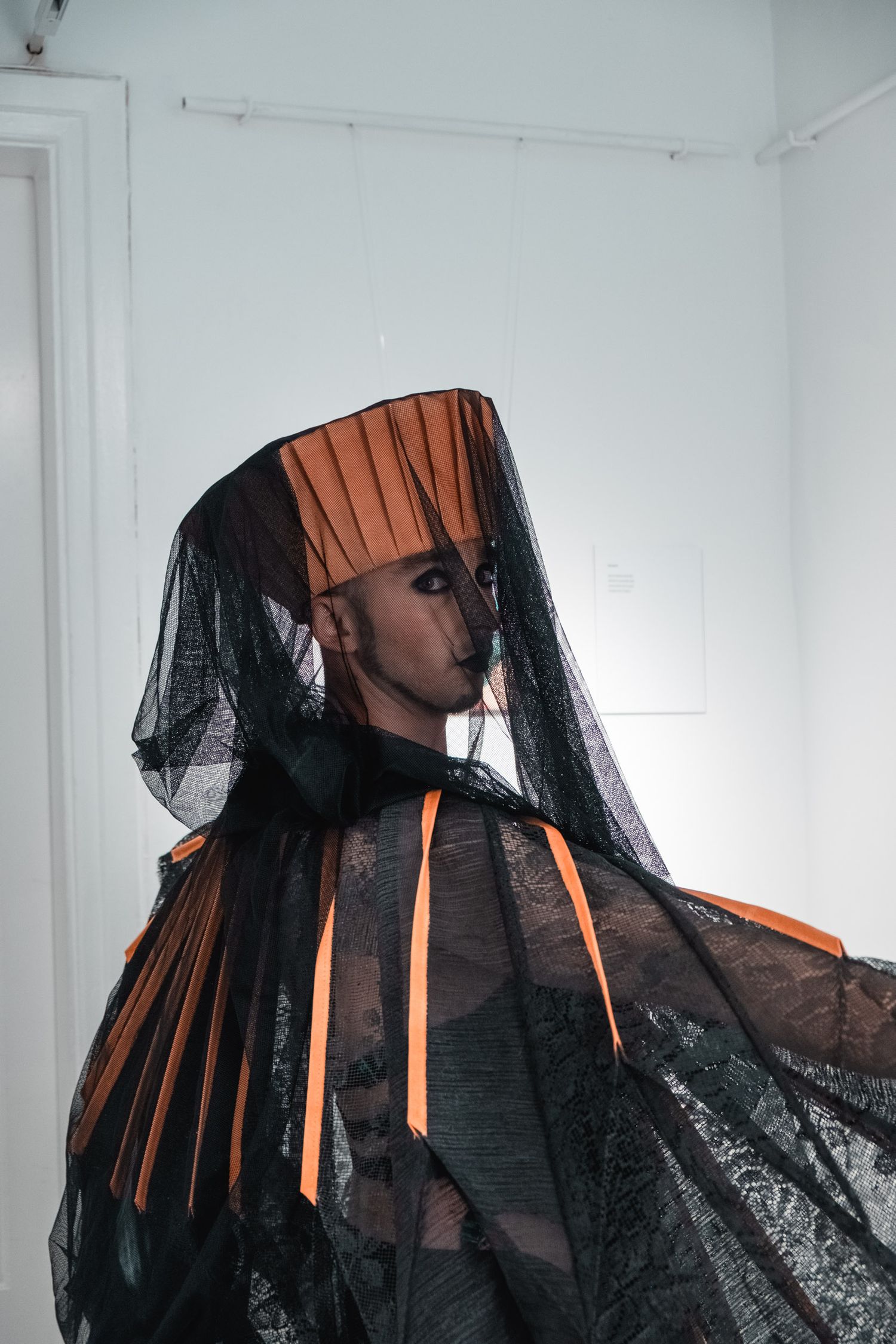 Artistic portrait with black veil and orange pleated details creating dramatic silhouette.