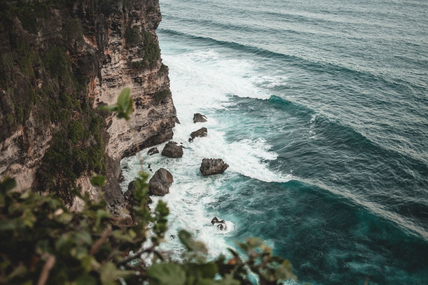 Rugged limestone cliffs meet crashing turquoise waves along tropical coastline.