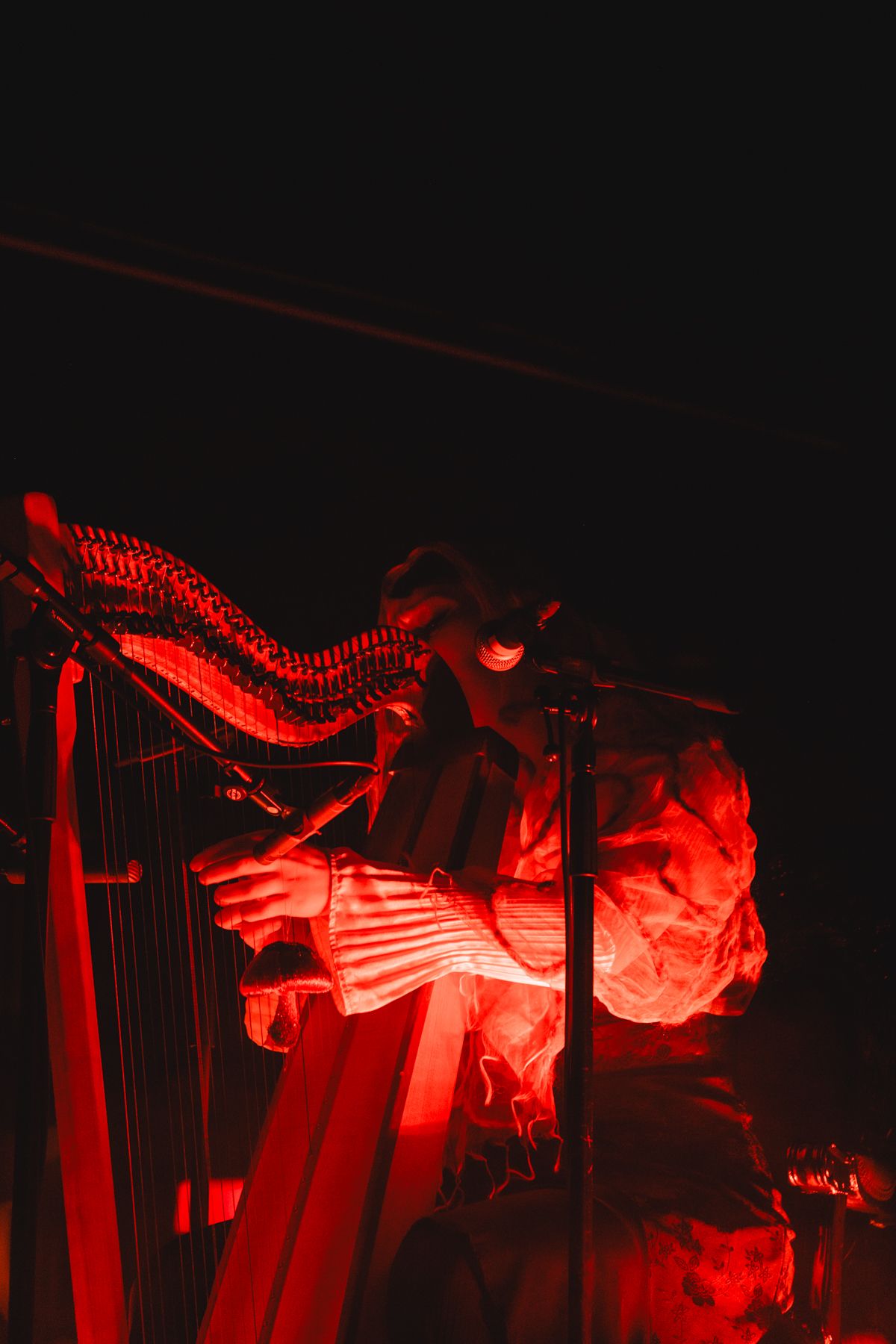 Harp player illuminated in dramatic red stage lighting during live performance.