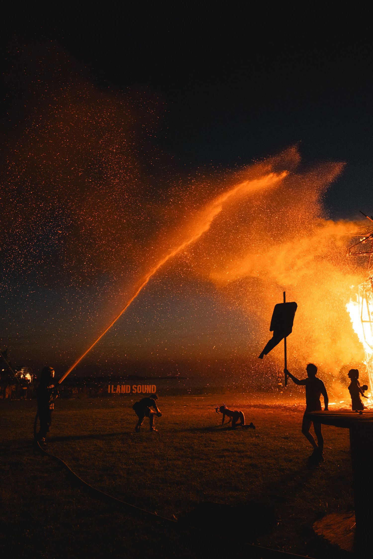 Orange water stream spraying through fire and smoke at night event.