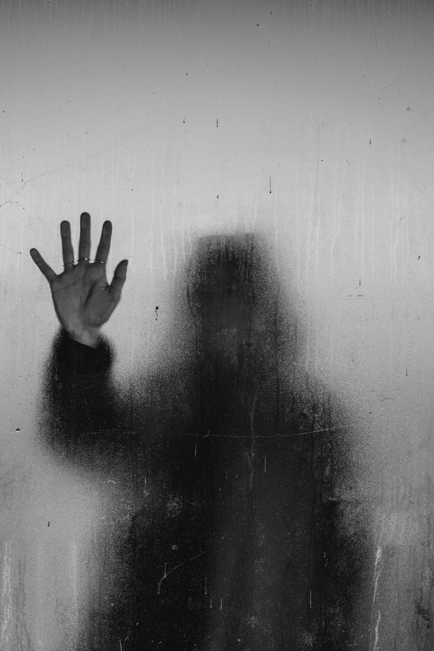 Silhouette of a hand pressed against frosted glass creates mysterious shadowy effect.