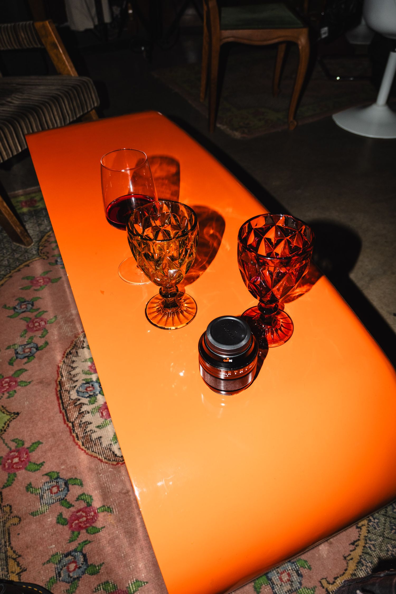 Vintage crystal glasses on an orange table surface casting dramatic shadows.