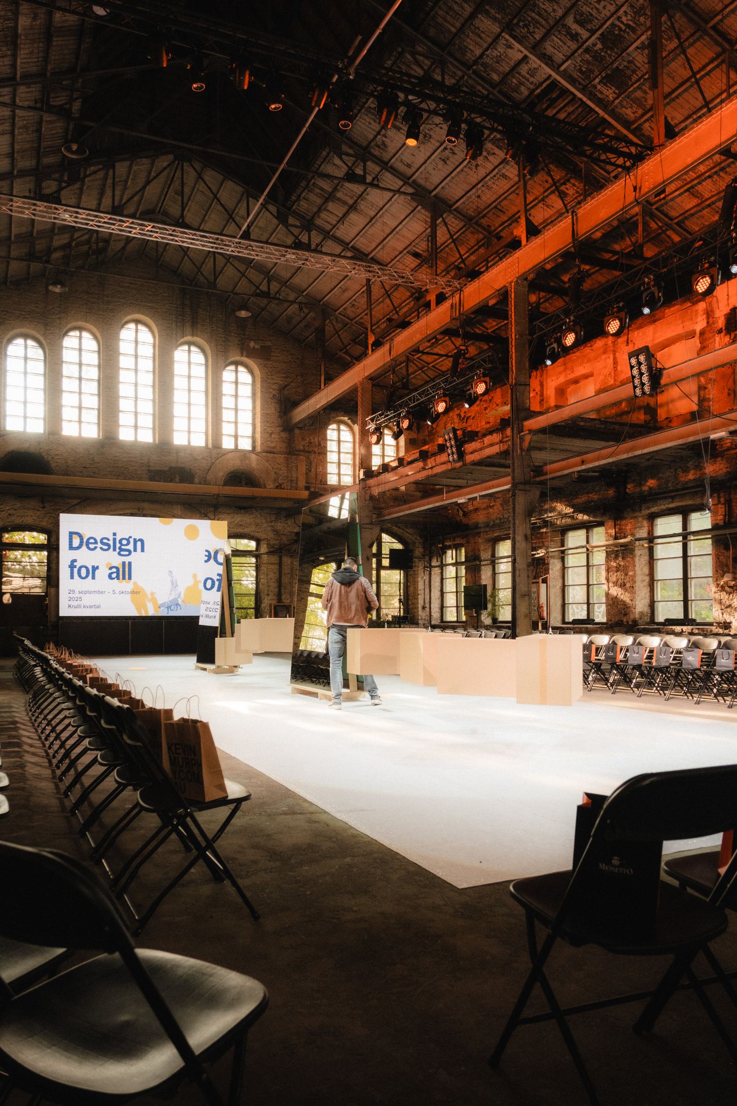 A panoramic view of an empty industrial event space with dramatic lighting and rows of chairs along the sides.