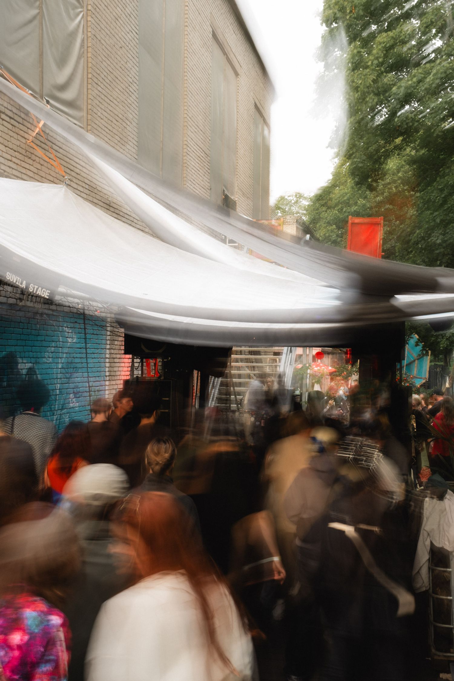 Blurred crowd of people moving under a white tent canopy at an outdoor event.