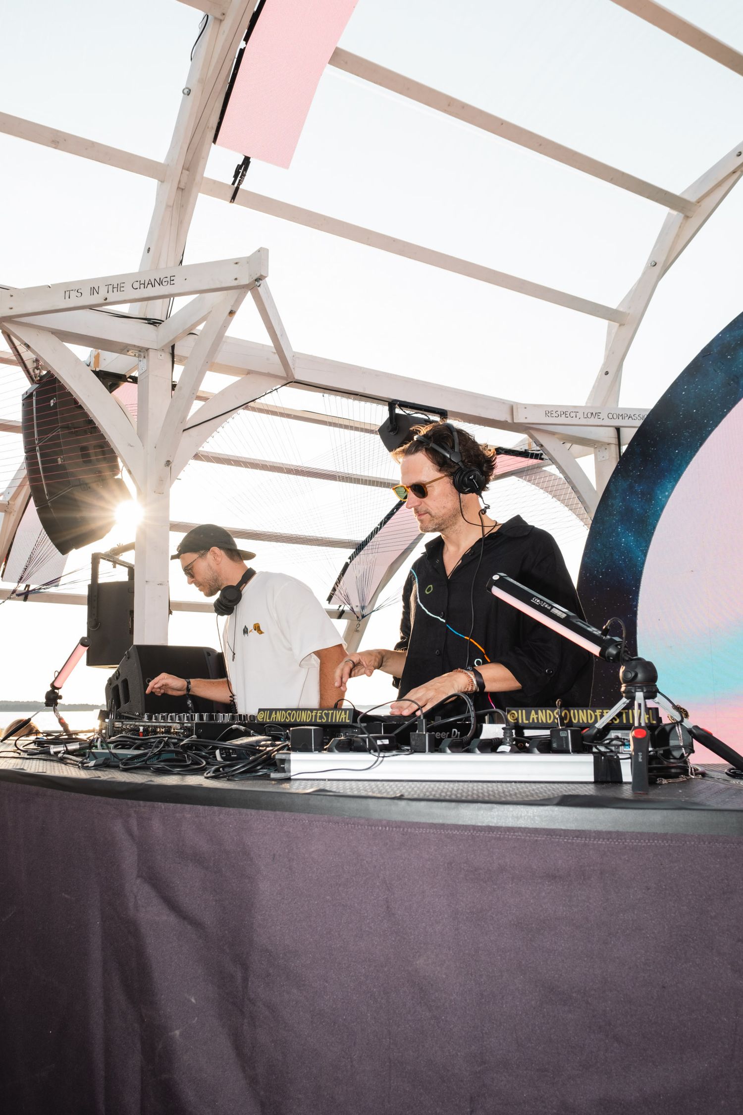 DJs performing at outdoor music festival under white tent structure.