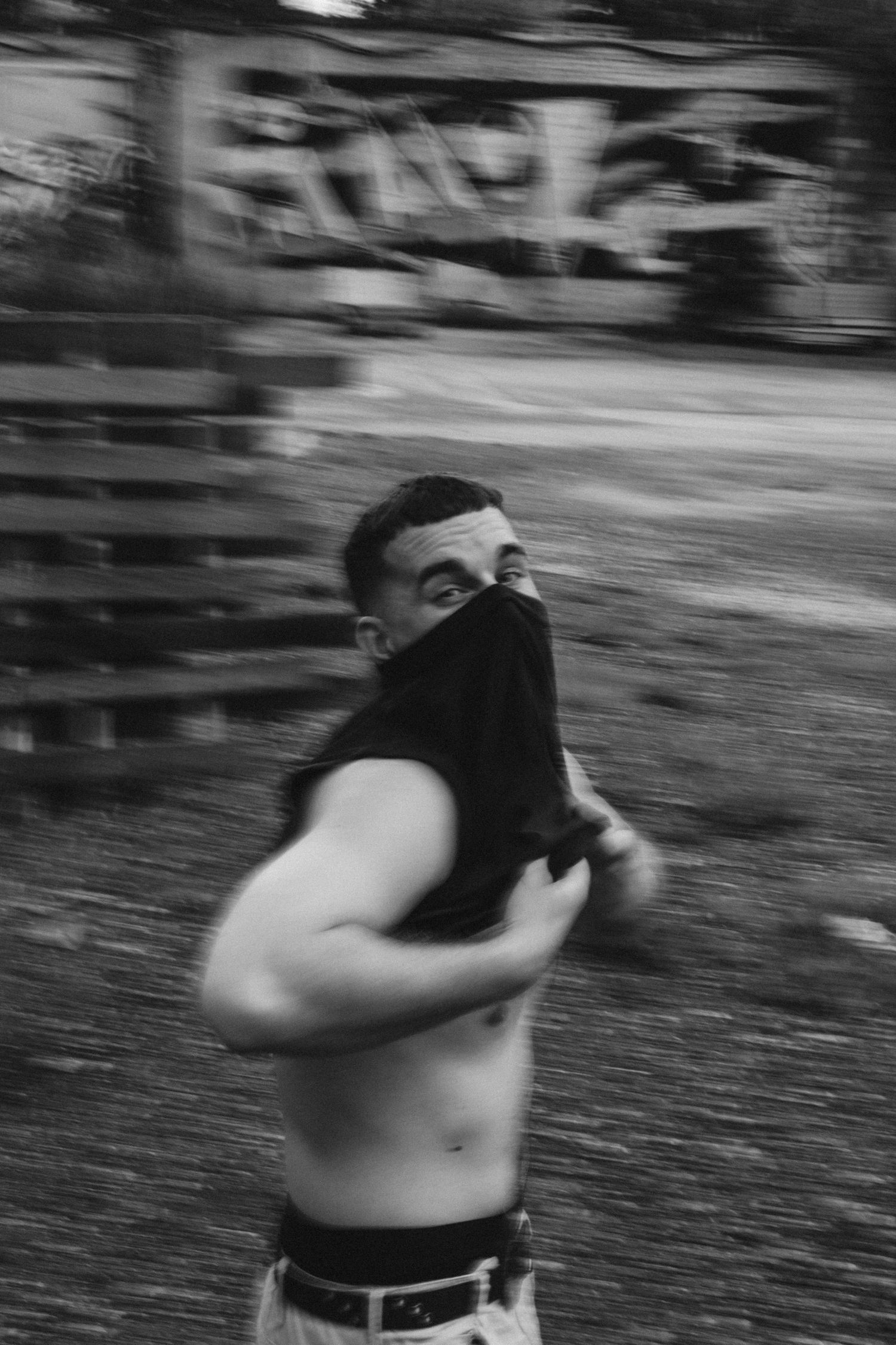 Dynamic black and white photo of person removing shirt with graffiti wall in background.