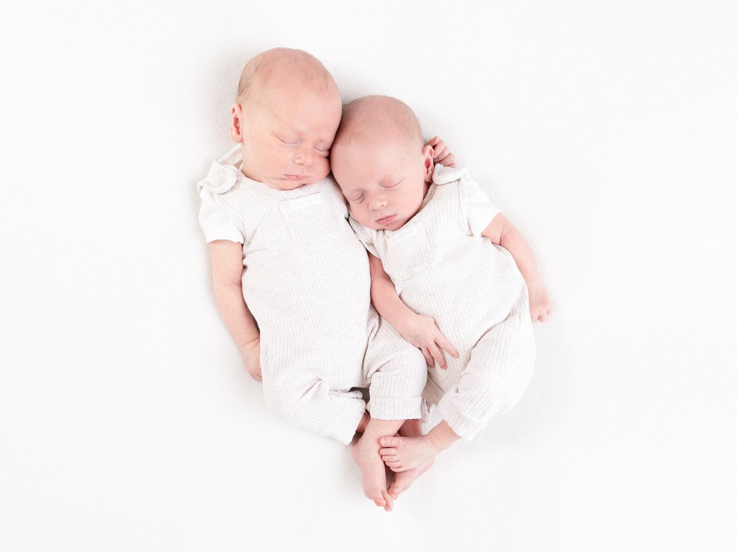Sweet newborn baby wearing white onesie sleeping peacefully on pink background.