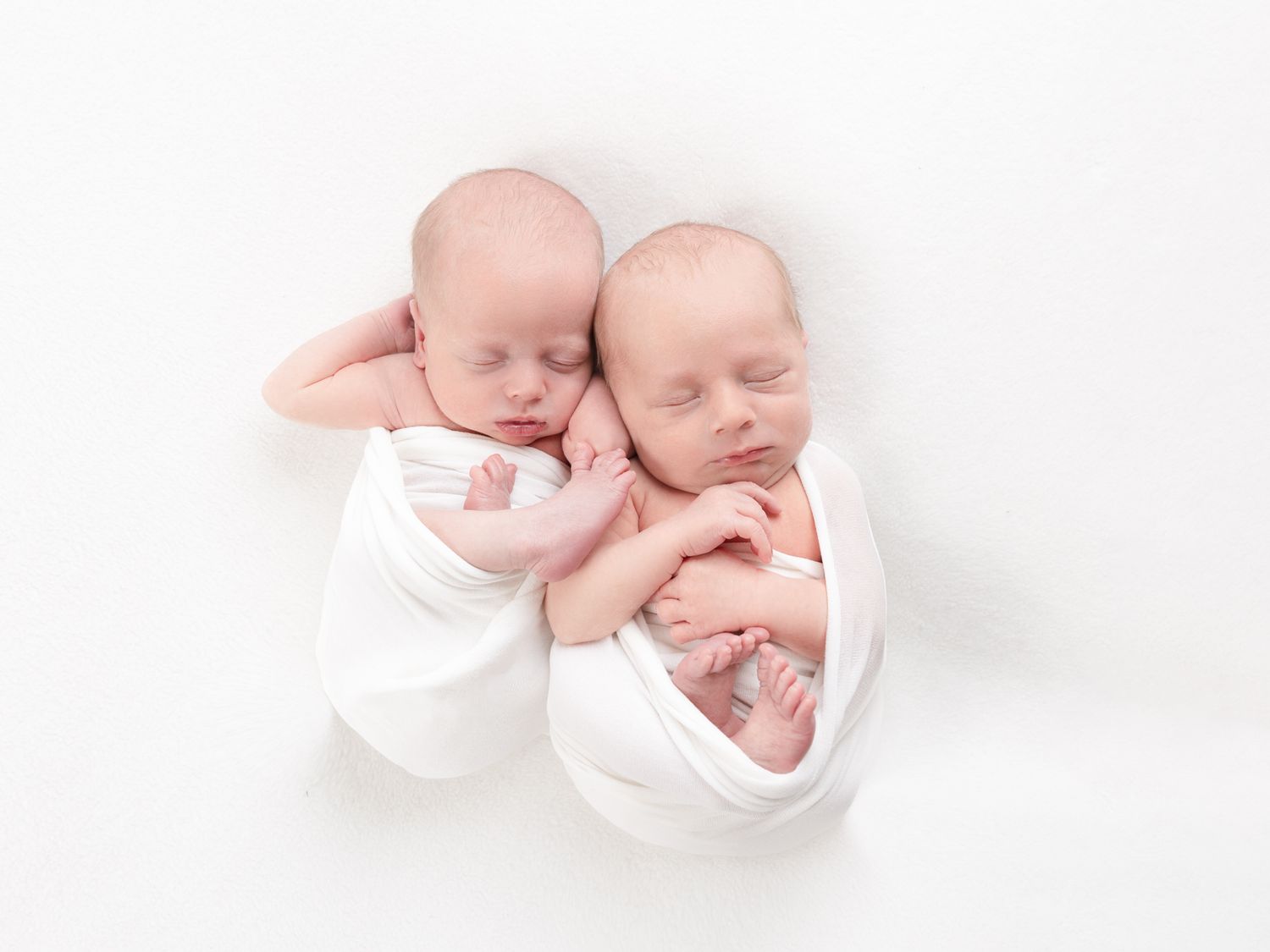 Two babies in white wraps sleeping side by side on white background.