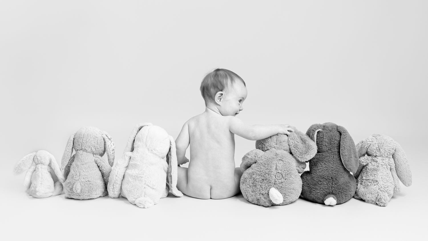 Minimalist baby photography with stuffed animals arranged on white background.