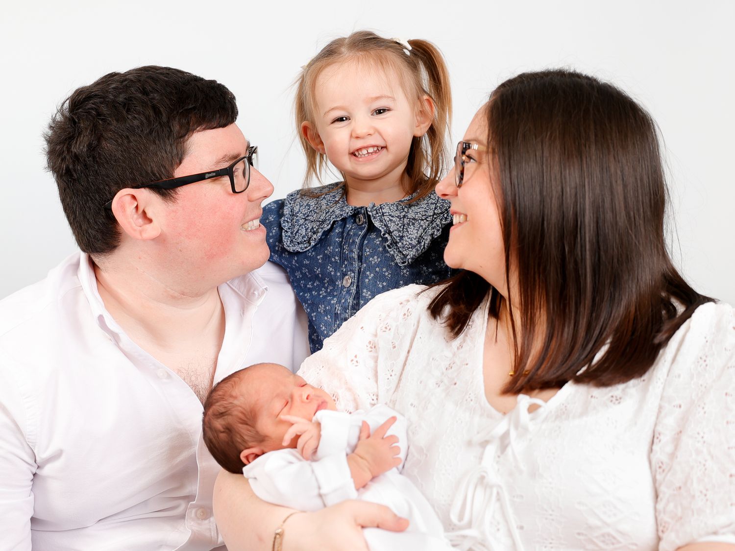 Happy family portrait with parents, toddler girl, and newborn baby on white background.