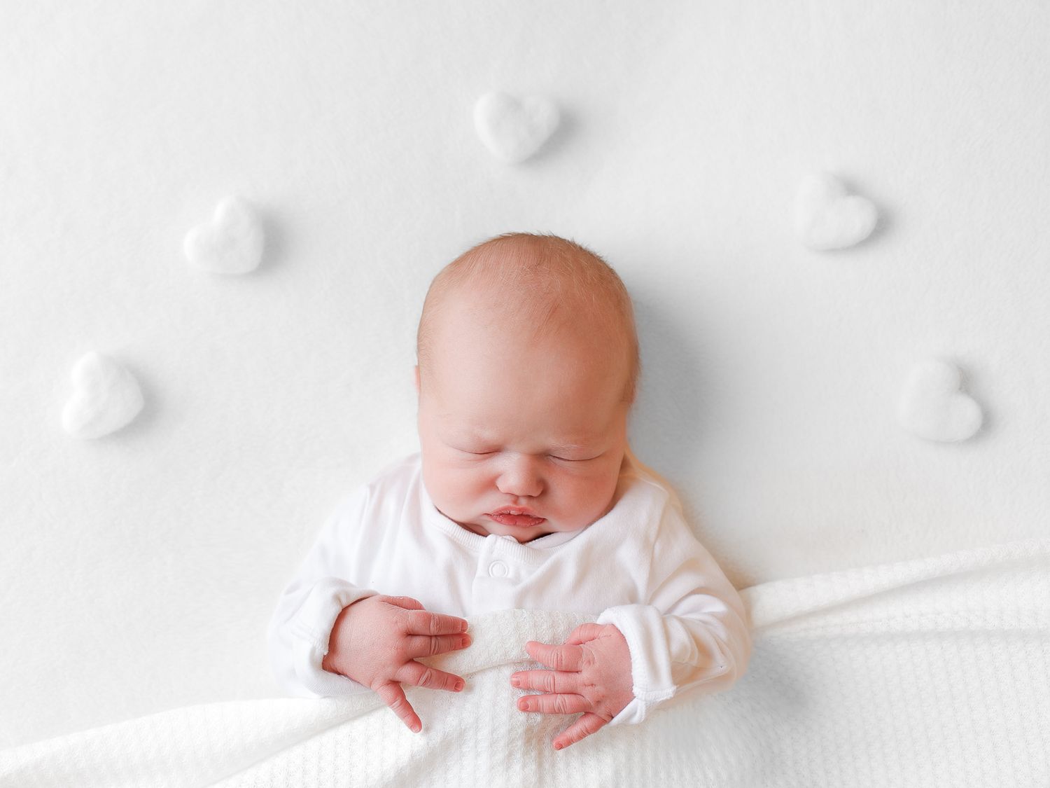 Newborn in white clothing sleeping on textured white background.