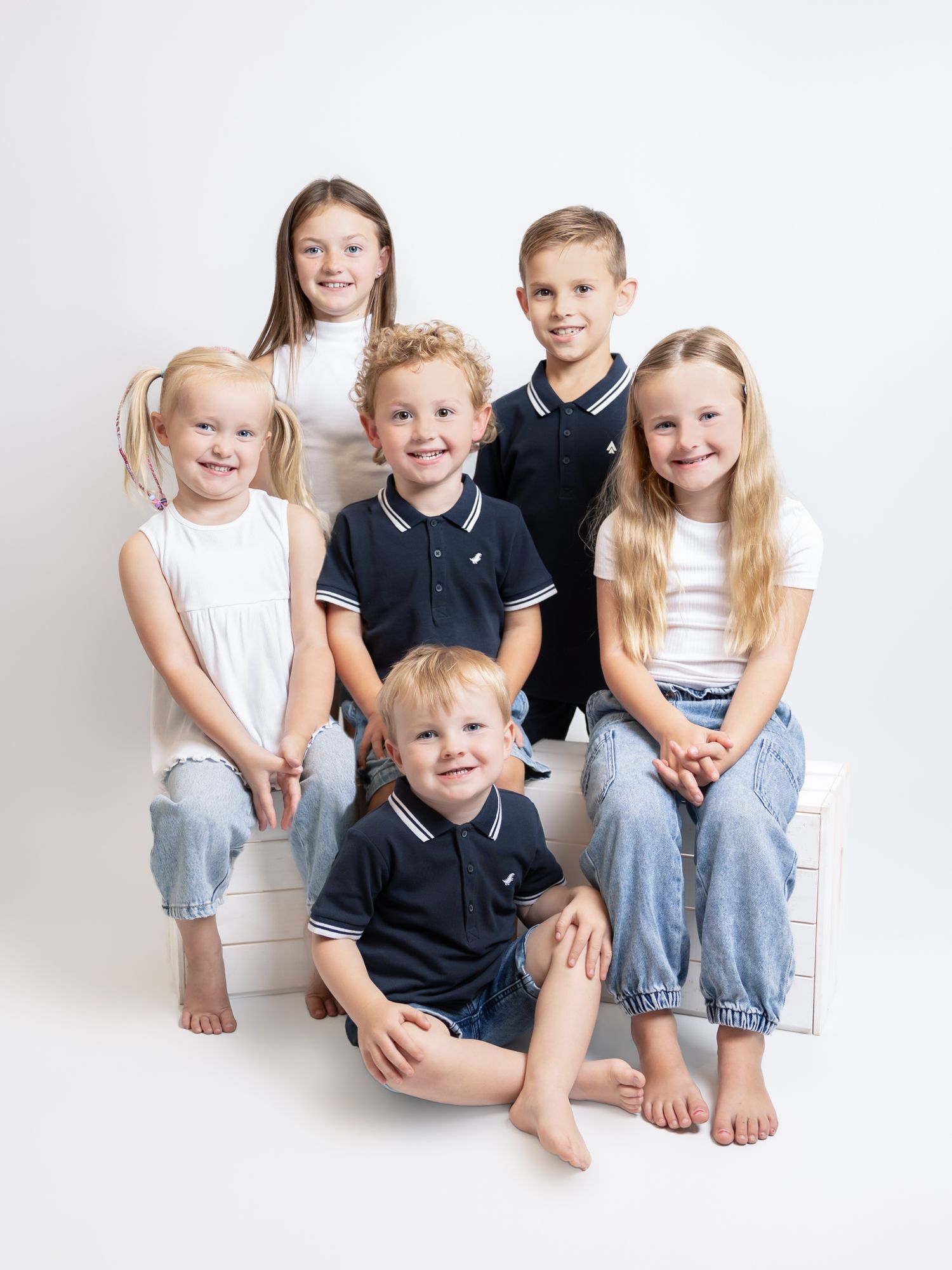 Group of children in casual clothing sitting together on white background.