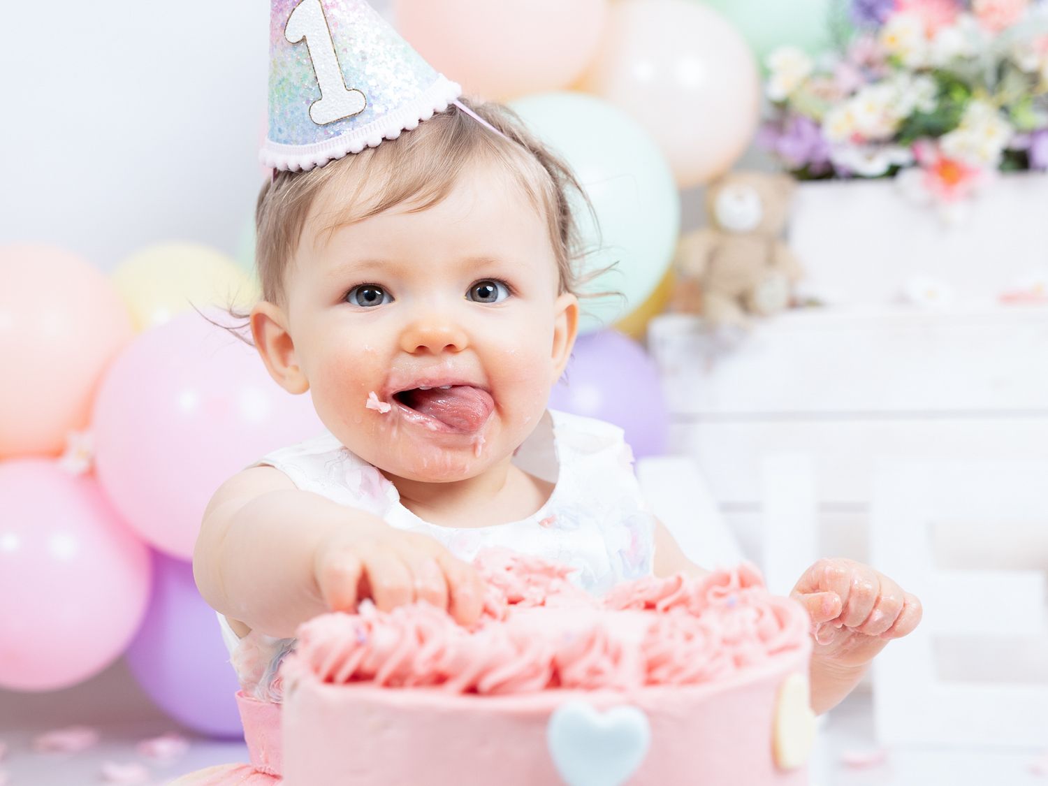 Colorful cake smash photography session featuring baby with pink frosting and pastel balloons.