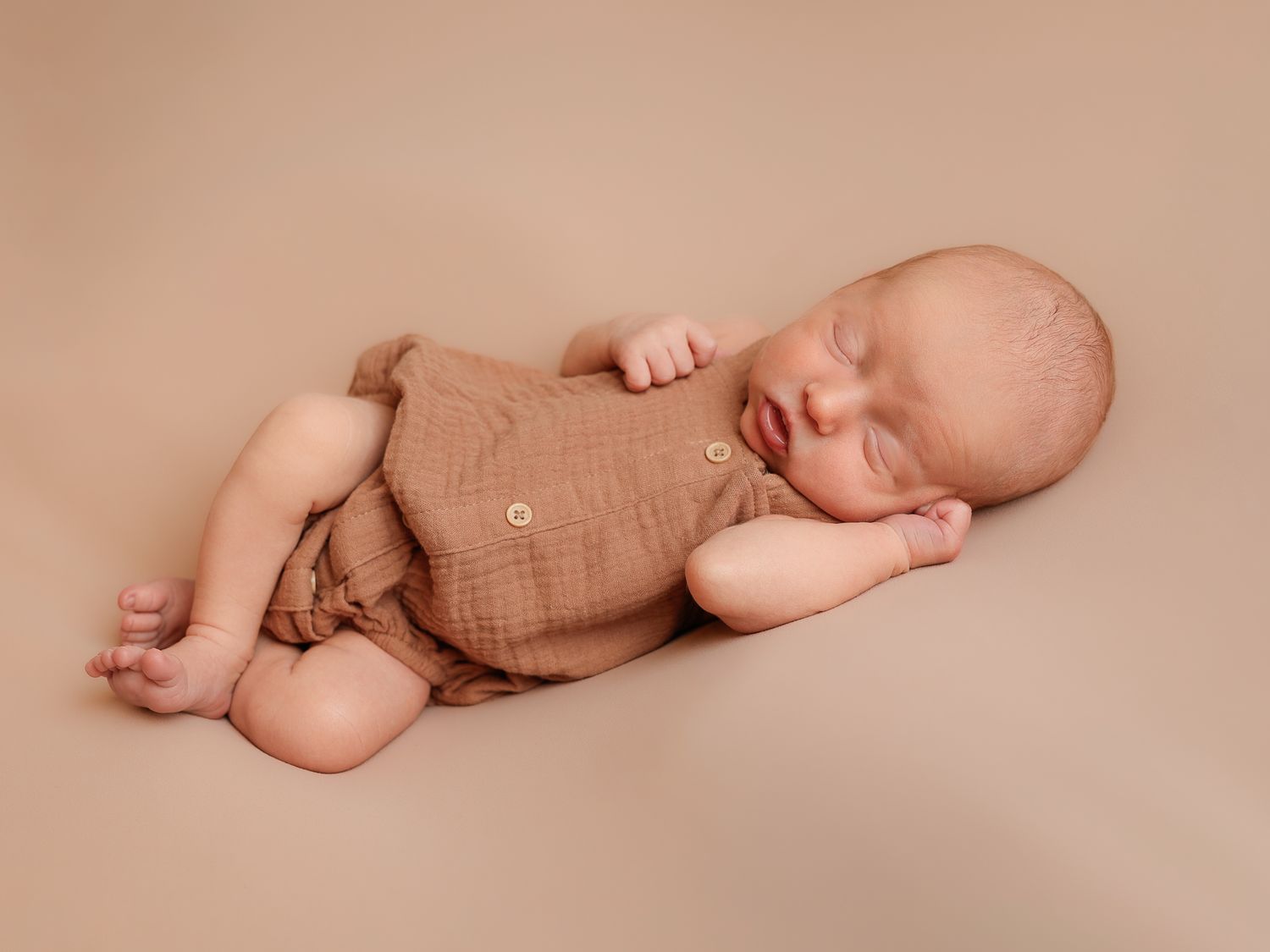 Newborn baby sleeping peacefully on neutral beige backdrop in minimalist style.