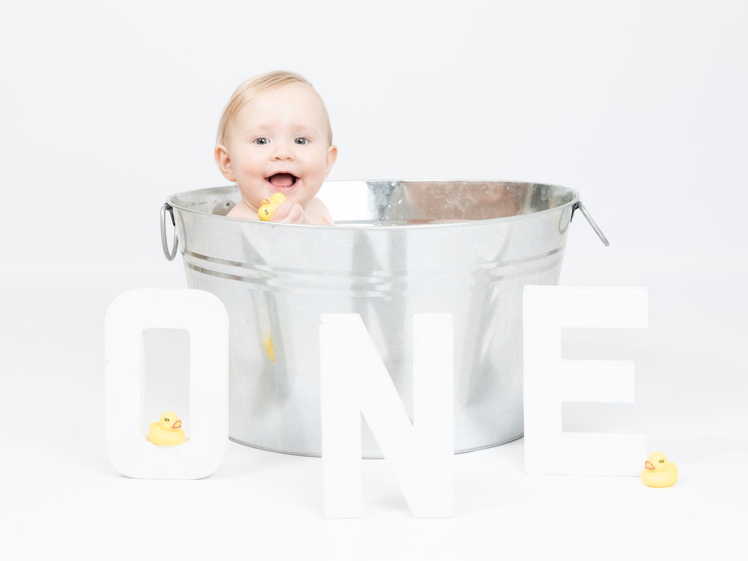 Baby bath photography setup with silver tub and minimal white background.