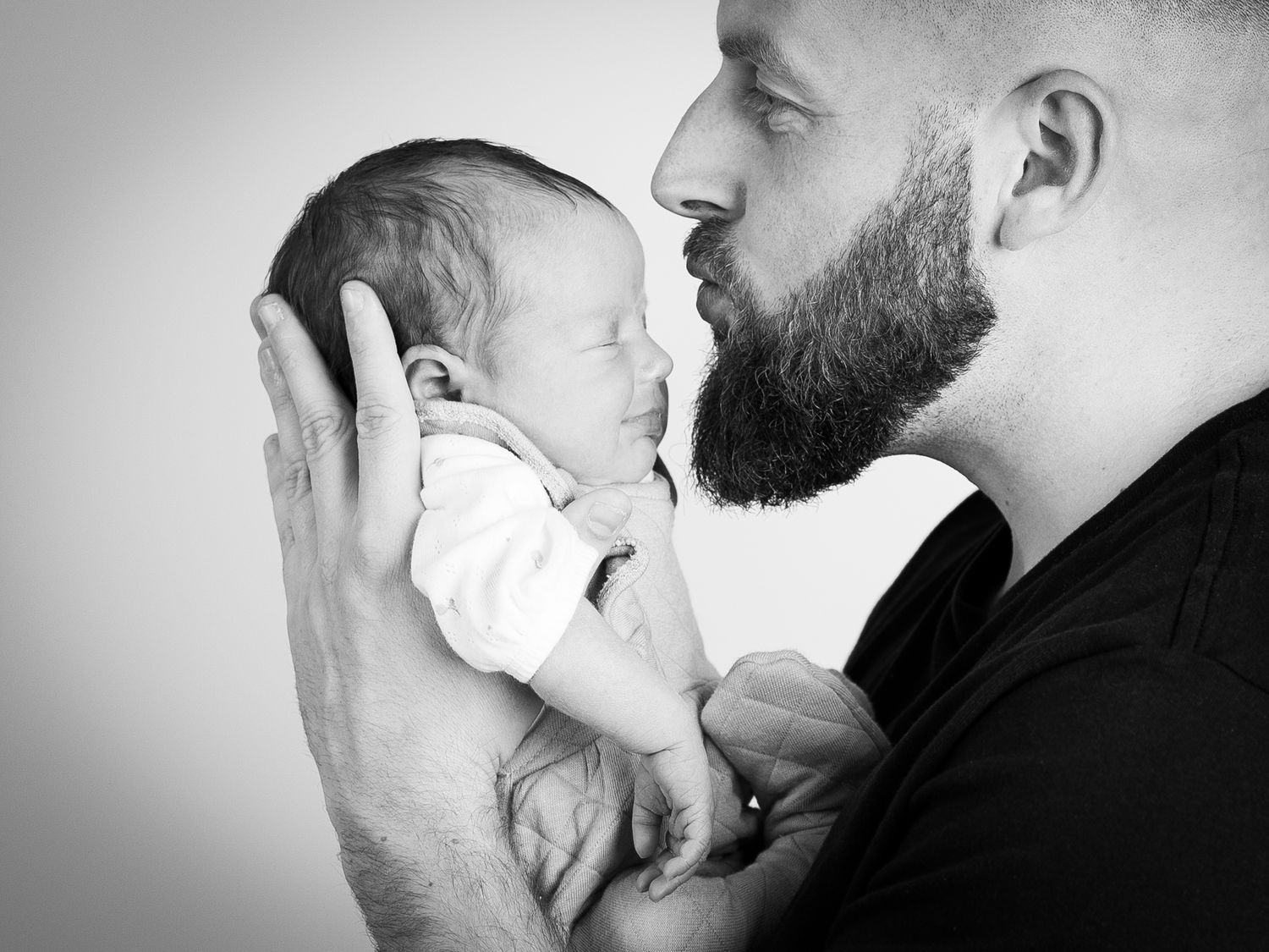 Black and white portraits showing tender moments between parent and newborn in studio setting.