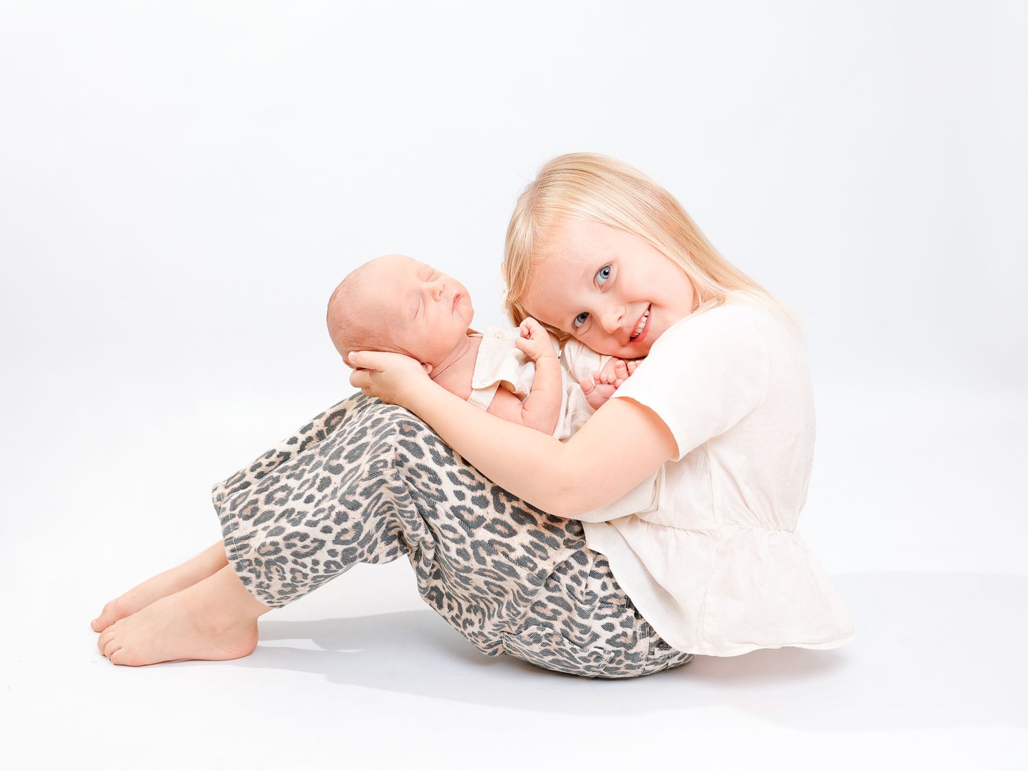 Newborn baby in leopard print pants lying on white backdrop in artistic poses.