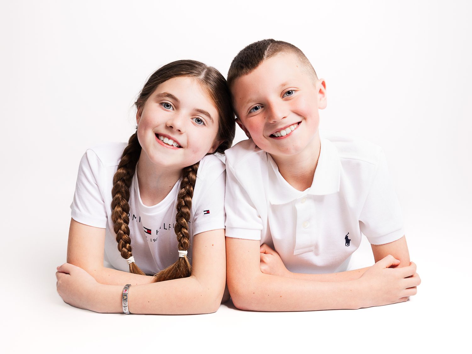 Siblings in matching white shirts posing together during professional photo session.