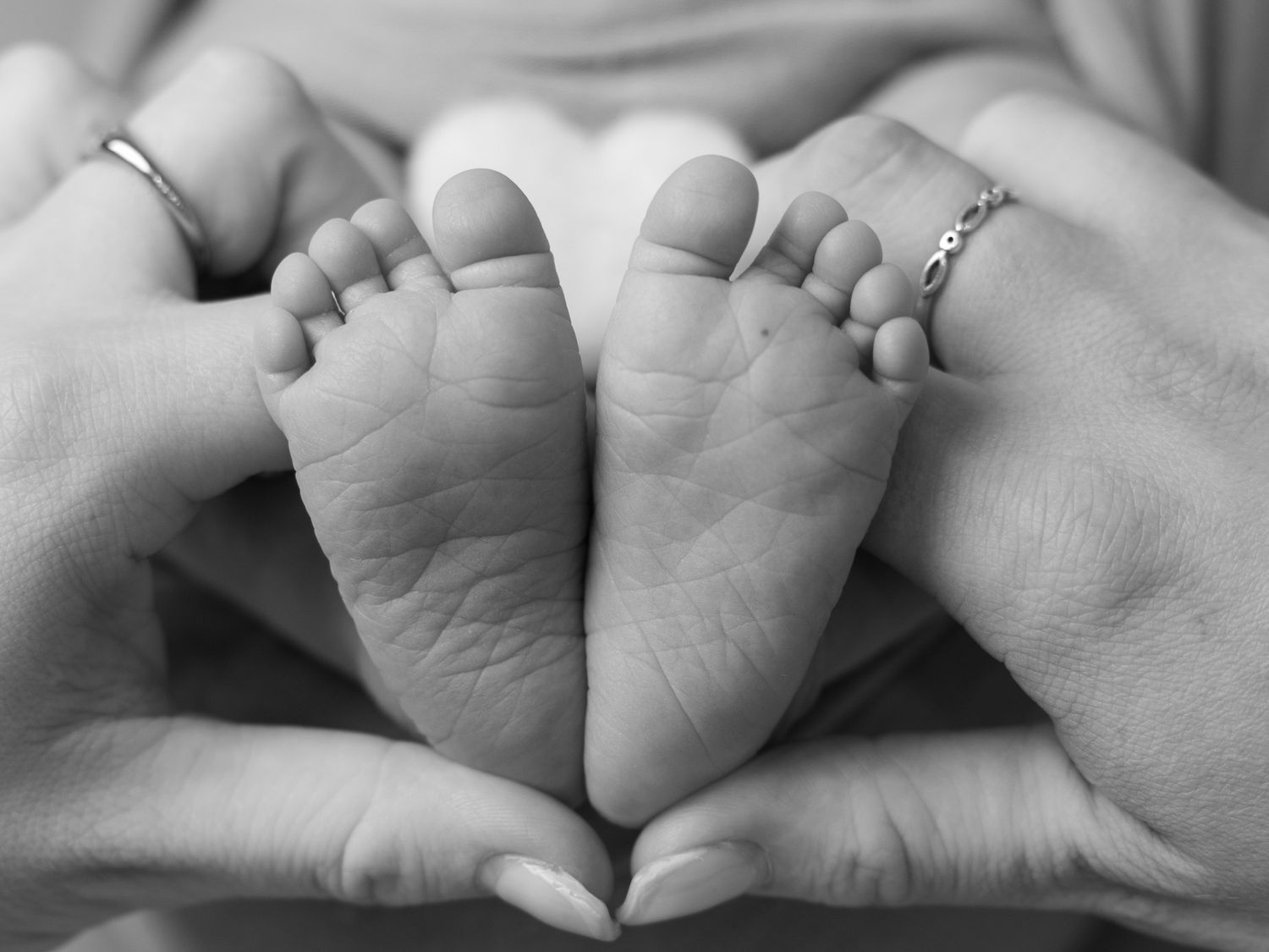 Black and white close-up of tiny baby feet with adult hands.