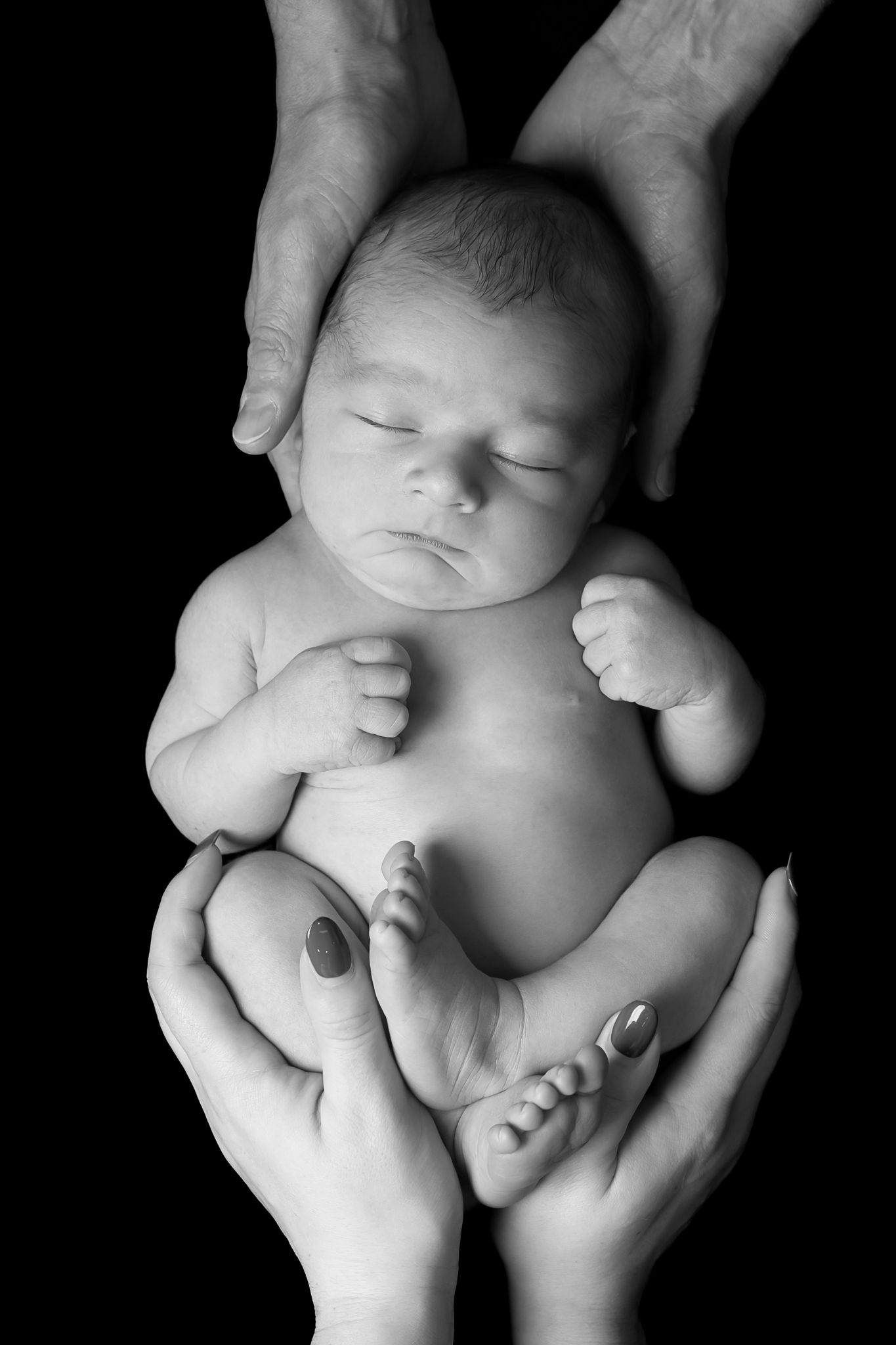 Artistic black and white portraits of a newborn baby cradled in hands against dark background.