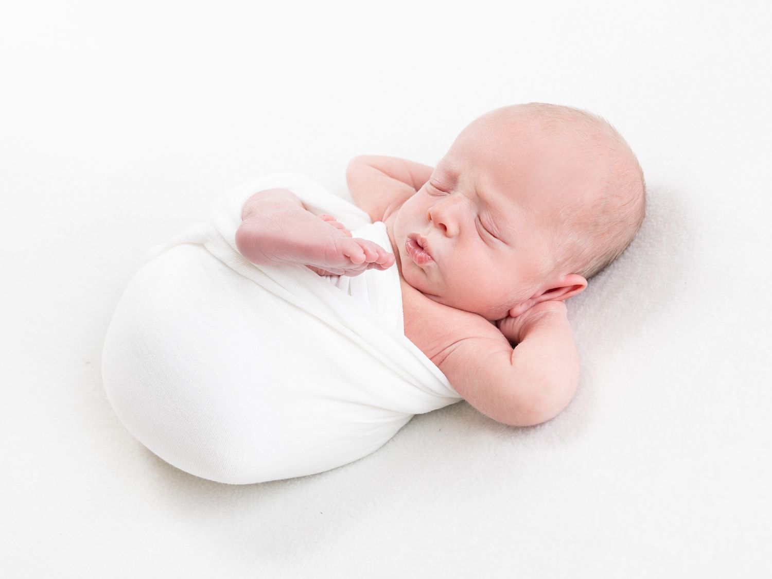 Peaceful sleeping newborn baby in white swaddle blanket against white background.