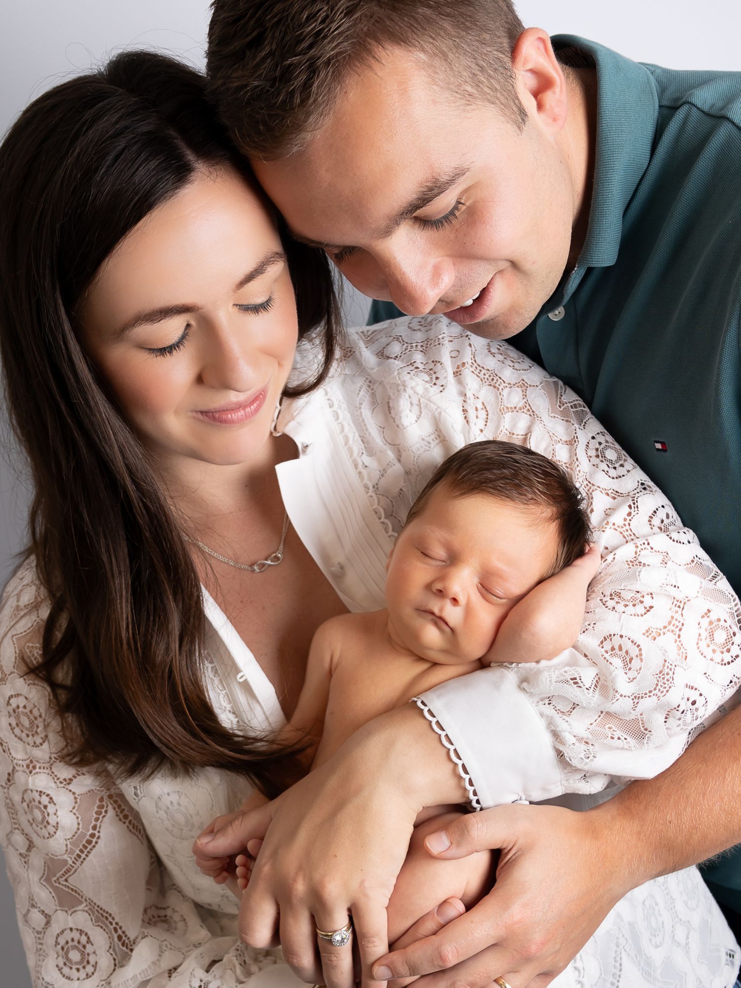 Parents in white and teal clothing sharing tender moments with their newborn baby.