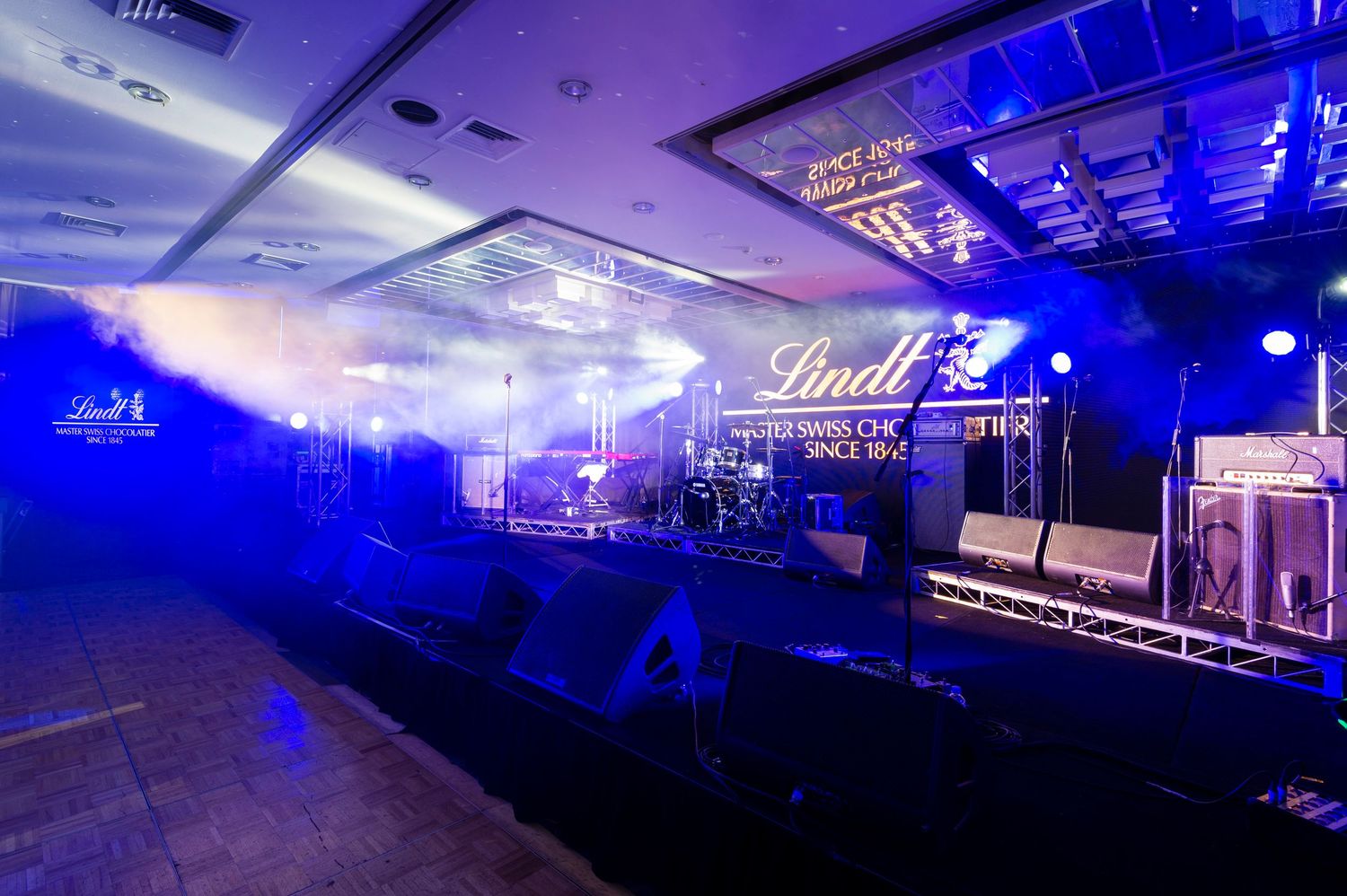 Concert venue illuminated with dramatic blue lighting and stage equipment visible in a panoramic view.