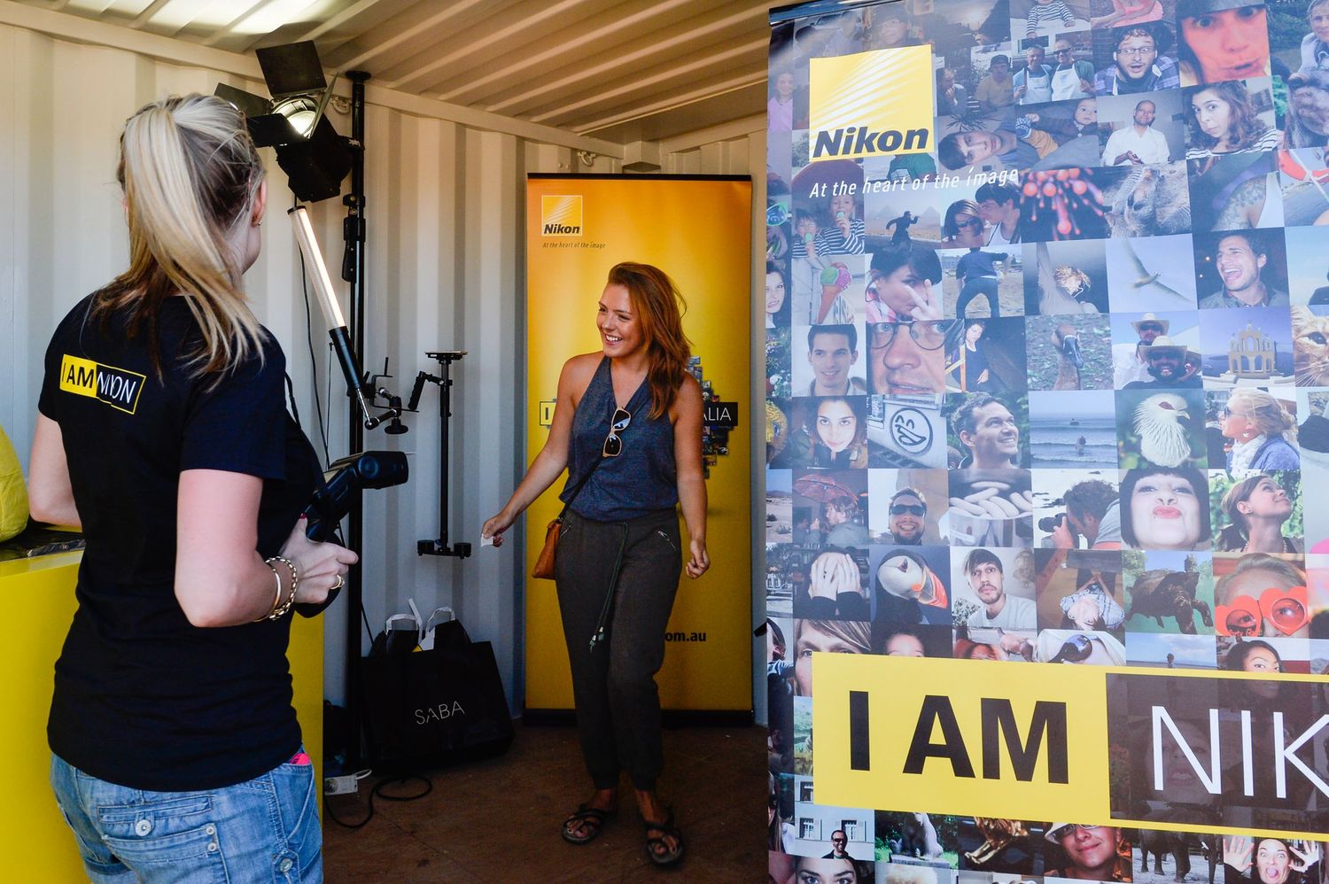 A camera operator films a scene next to a wall covered with photos and an 