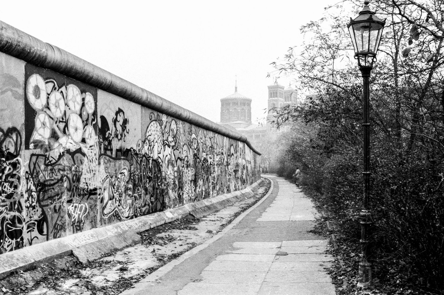 Graffiti covered Berlin Wall stretching into the distance with lampposts along its length.