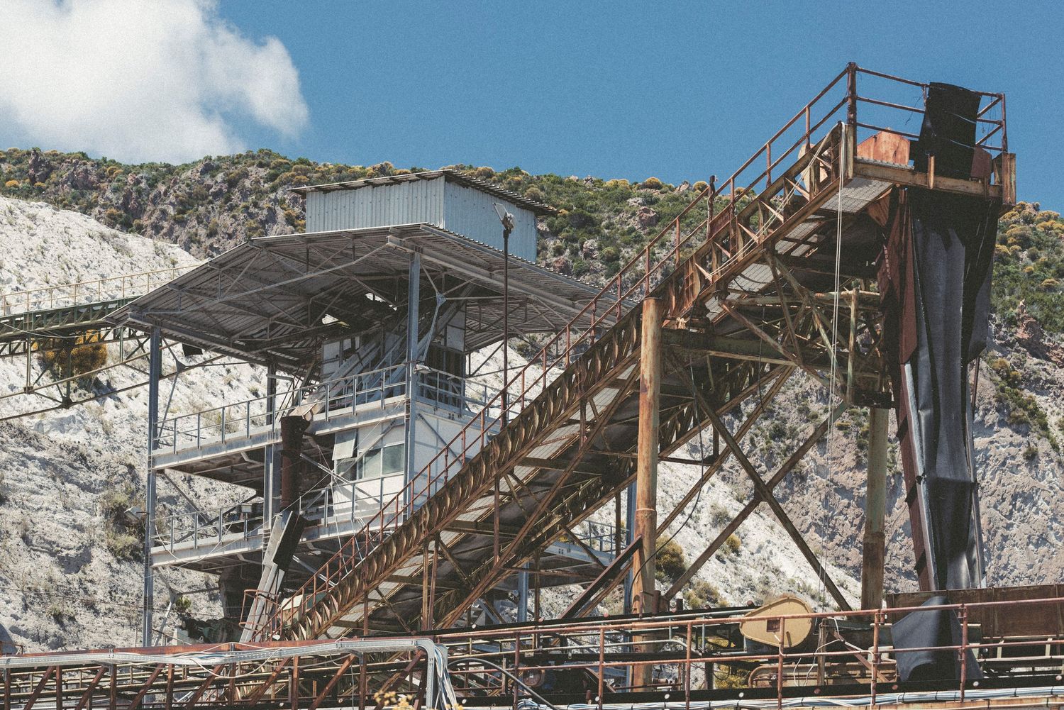 Abandoned industrial mining equipment and rusty metal structures against a cloudy sky at an old quarry site.