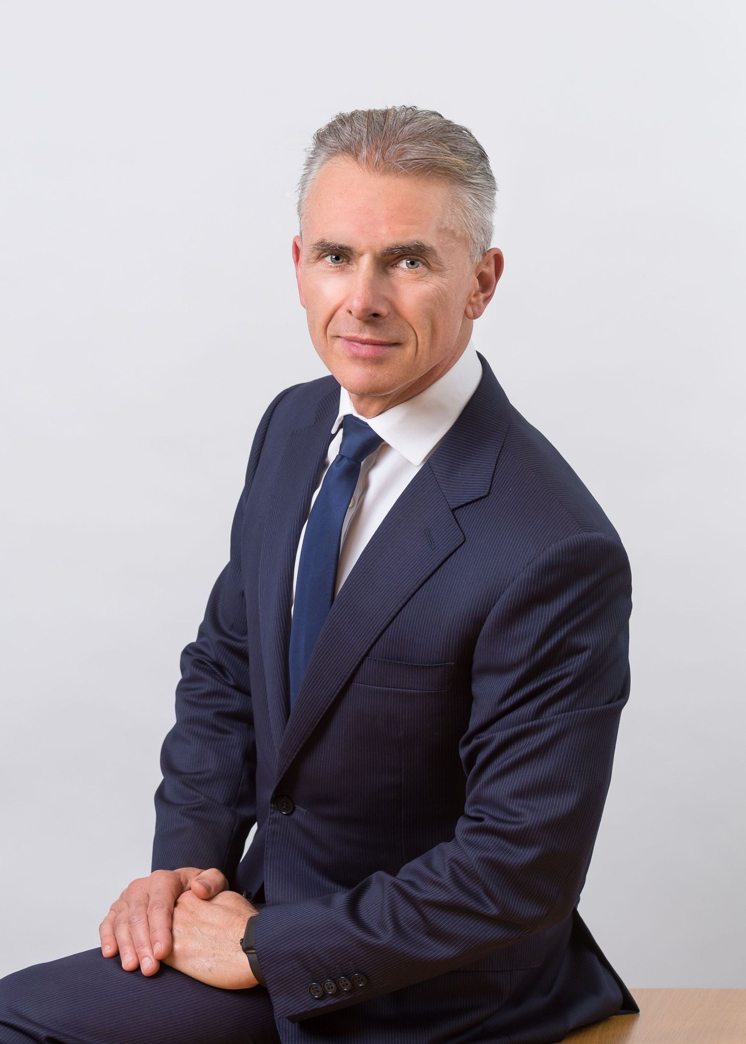 Professional headshots of person in navy suit and blue tie against white background.