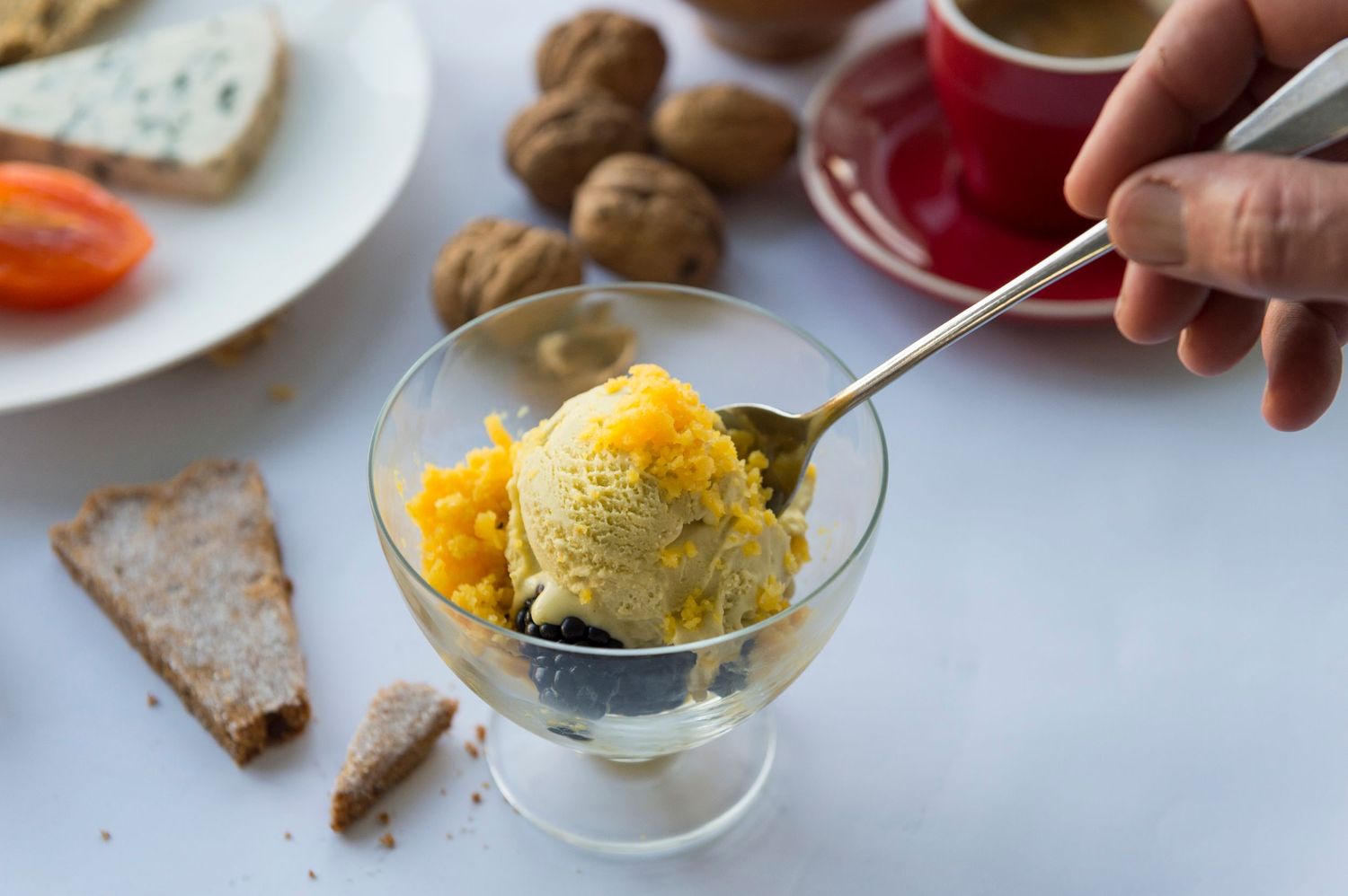 Hand scooping yellow sorbet or ice cream from small glass bowl.