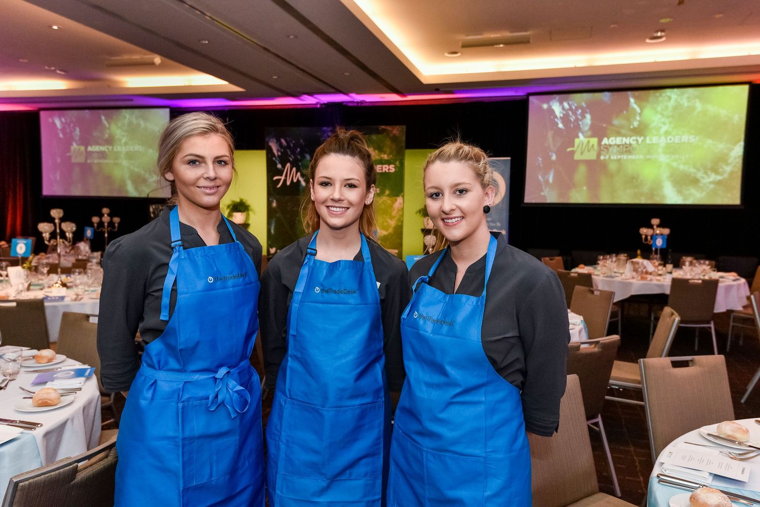 Staff members in sponsored blue aprons serving at an indoor corporate event at Rydges Resort Hunter Valley.