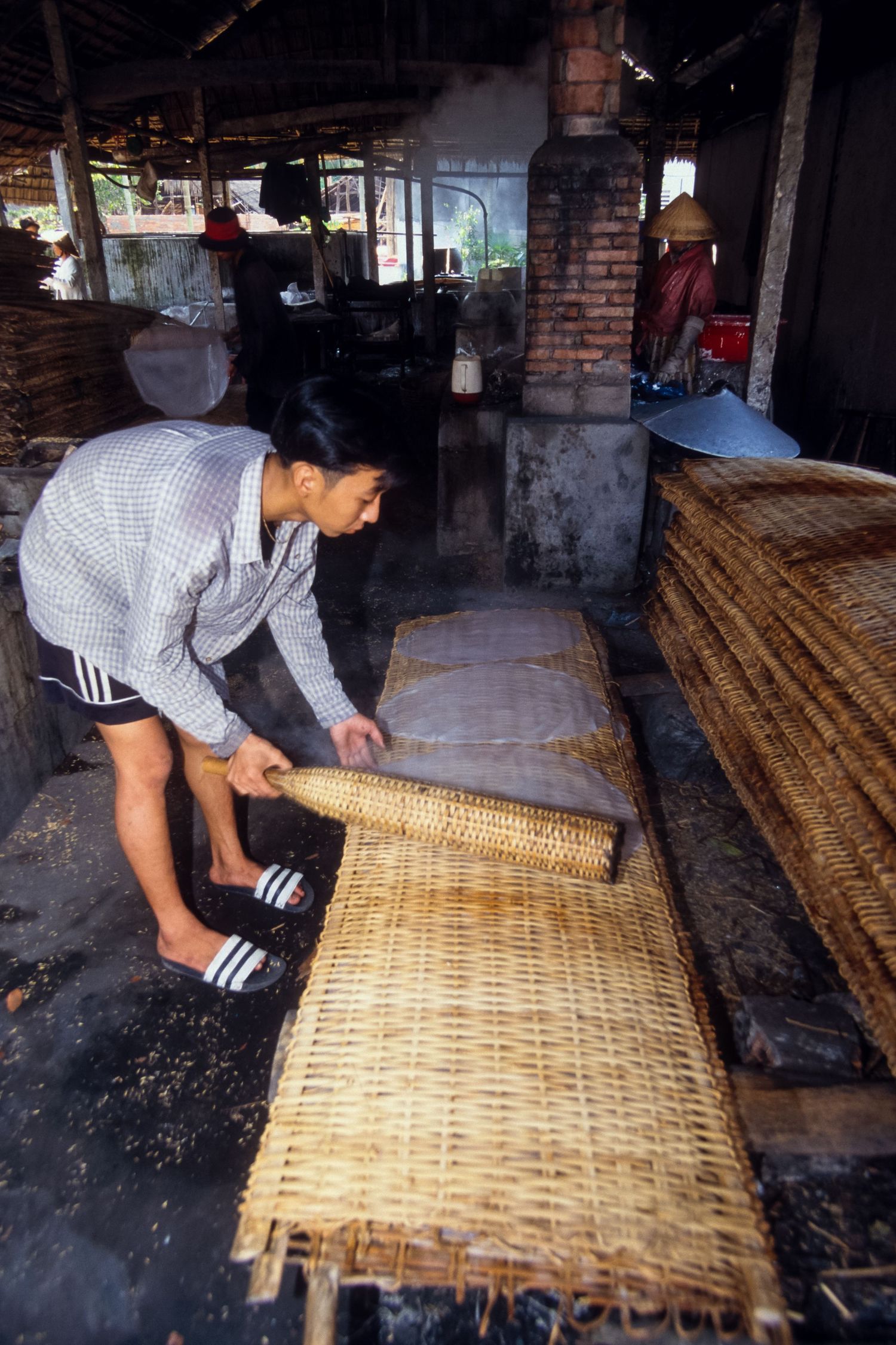 Craftsperson weaving a large bamboo mat on a traditional workshop floor.