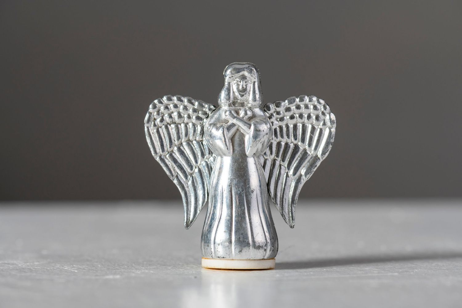 Glass angel Christmas ornaments with delicate wings displayed in a row on a light gray surface.
