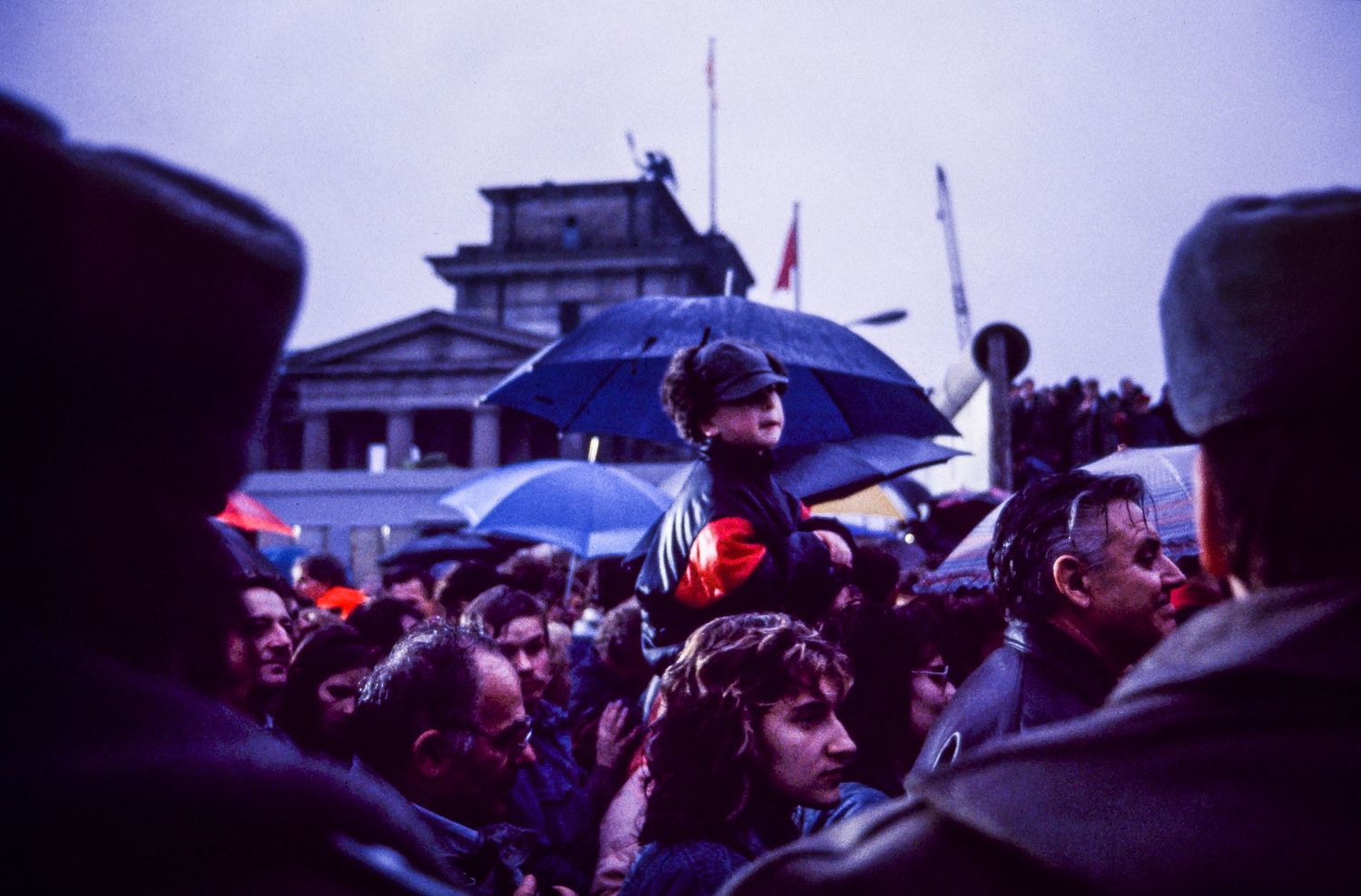 Crowd holding umbrellas gathered in the rain with dark silhouettes against evening sky.