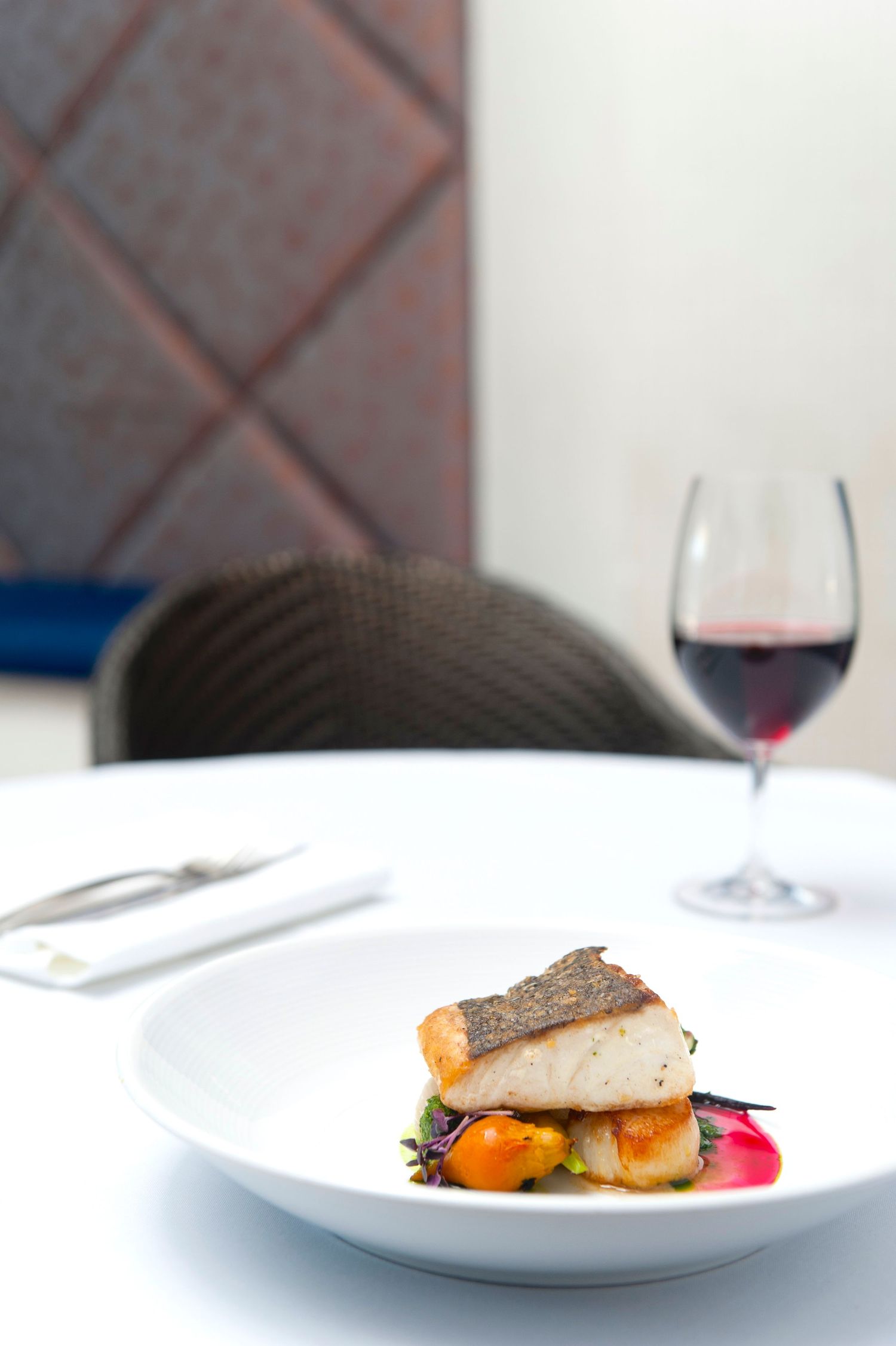 Plated fish dish with colorful garnishes served on white plates in an upscale restaurant setting.