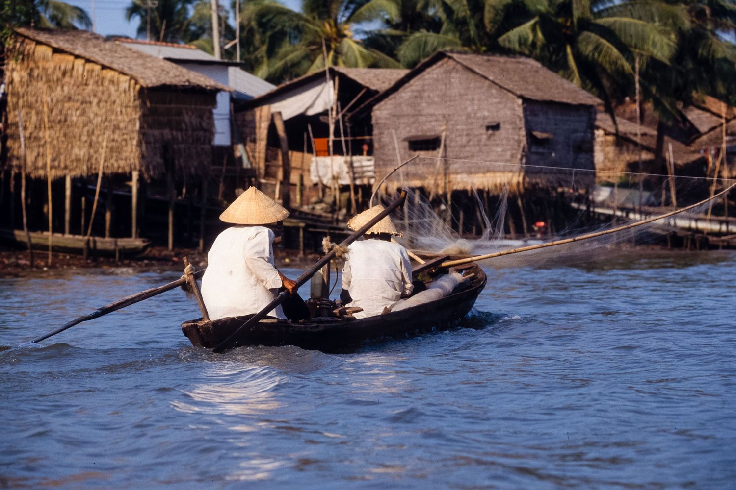 Traditional wooden boats navigate through a village built on stilts over water.