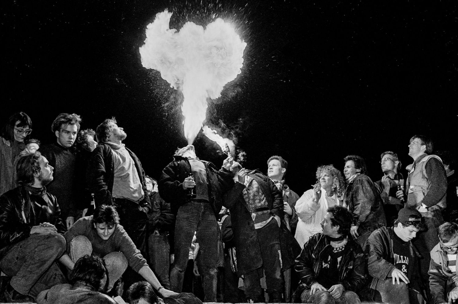 Crowd of people gathering at night along the Berlin Wall during historic events.