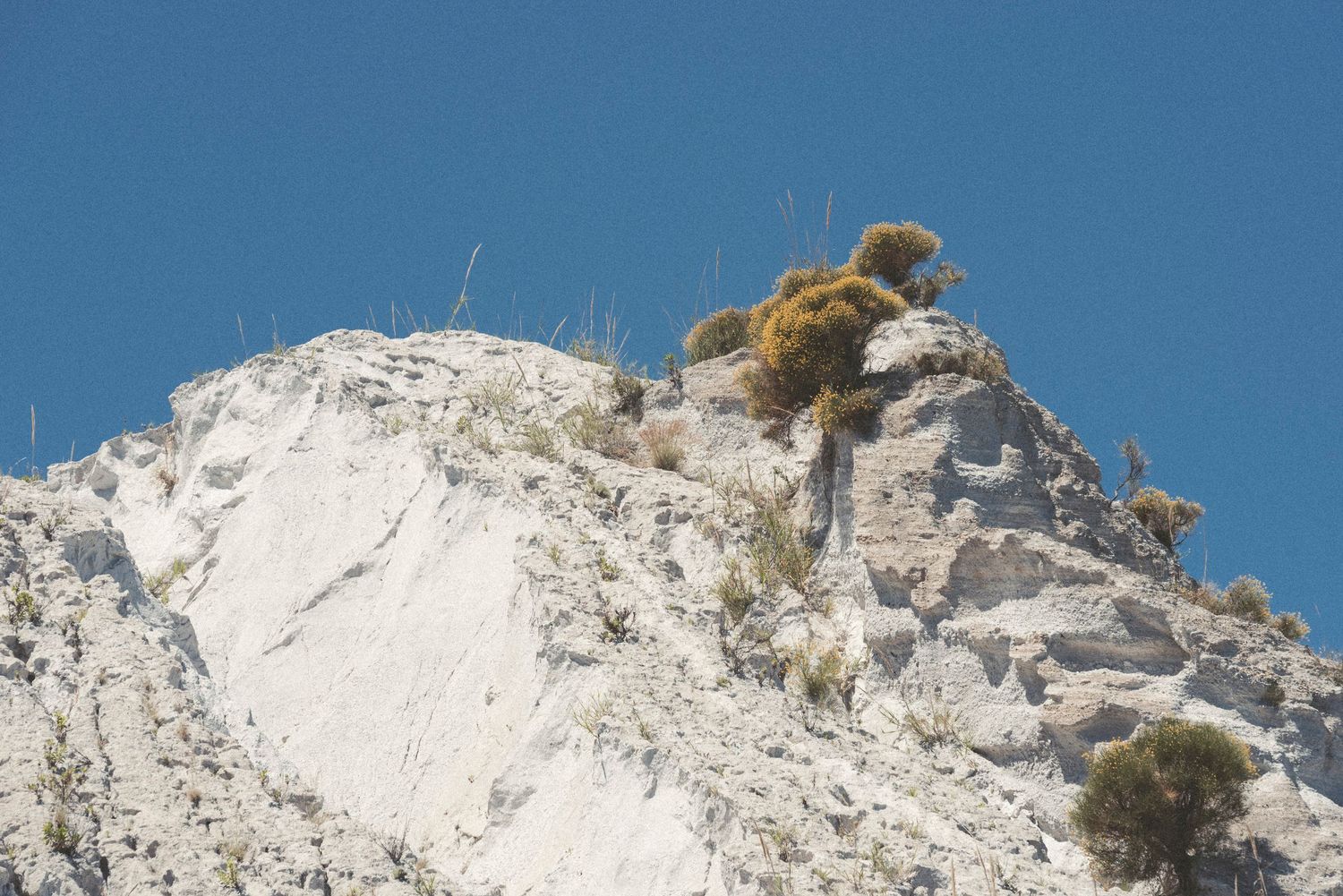 Aerial view of steep white limestone cliffs and rocky outcrops against a bright blue sky.