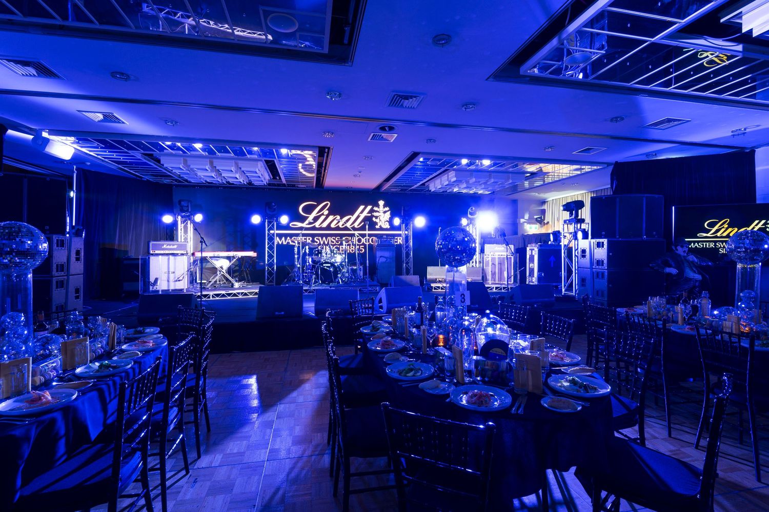 Elegant banquet hall with blue lighting and Lindt branding illuminated on walls, set for formal dining event.